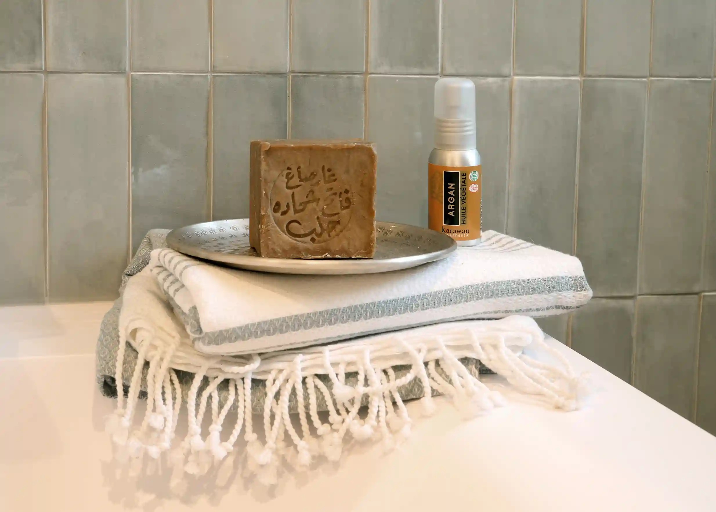 Fouta au coloris Mirage vue de près, dans une salle de bain avec un savon d'Alep et de l'huile d'argan