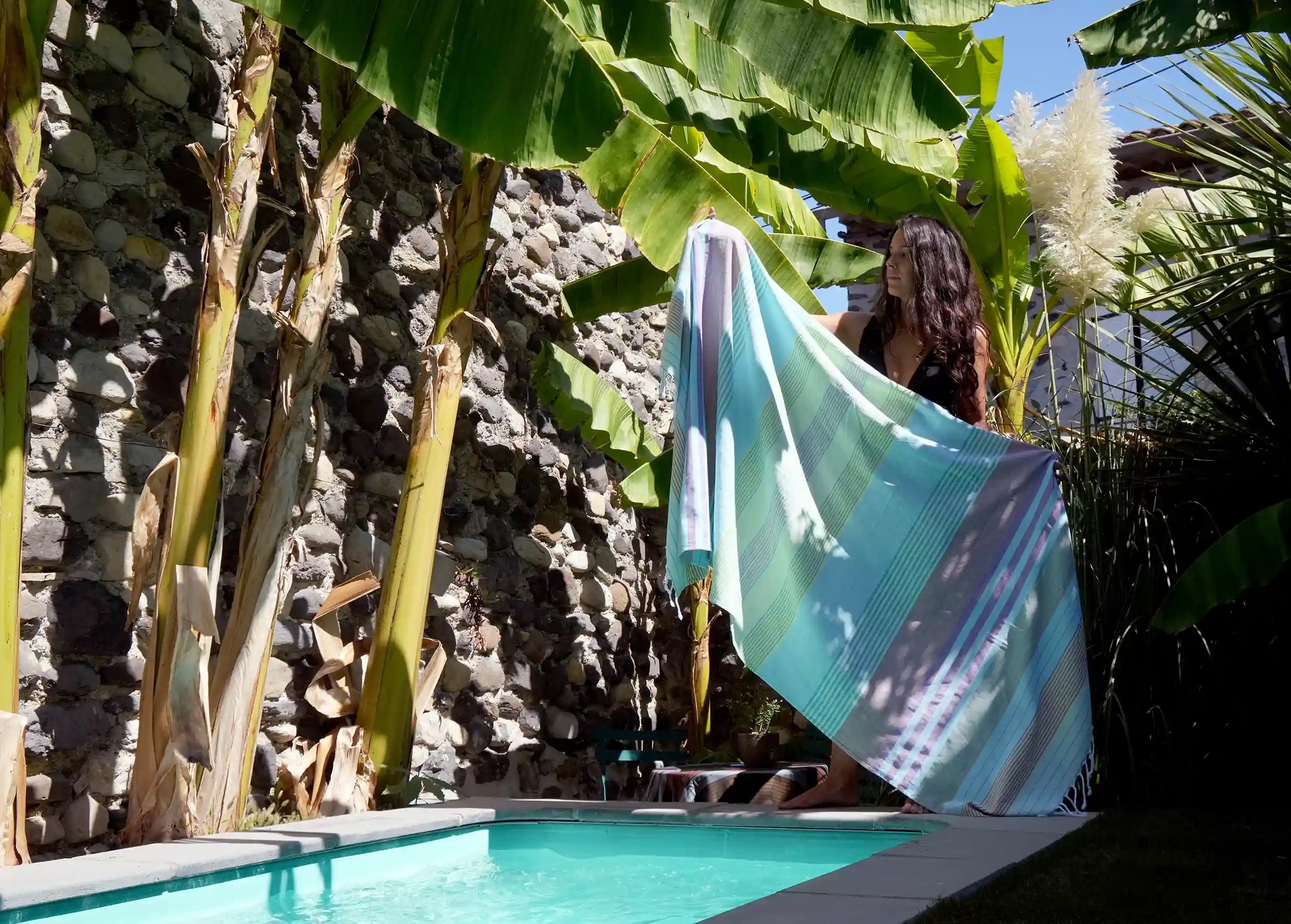 Fouta au coloris Aqua, collection Sud, tenue entre les mains par une femme, faisant paraître ses rayures multicolores