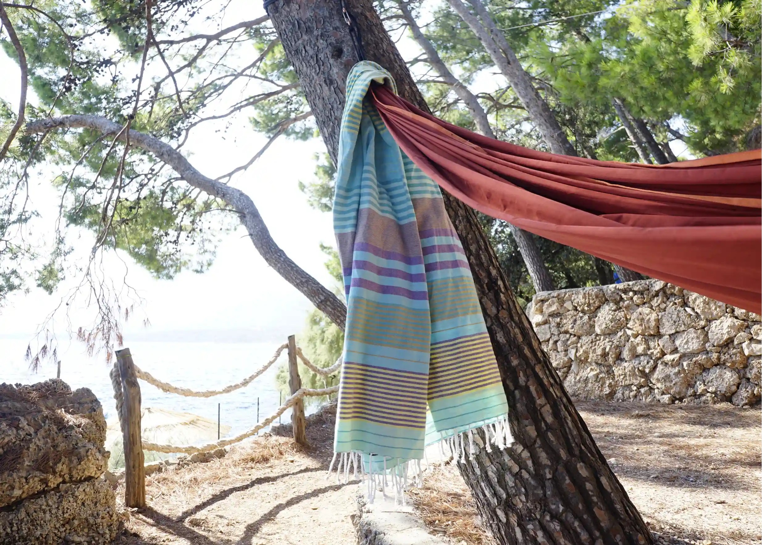 Aqua-coloured organic cotton fouta, Sud collection, hanging from a tree branch, the sea on the horizon