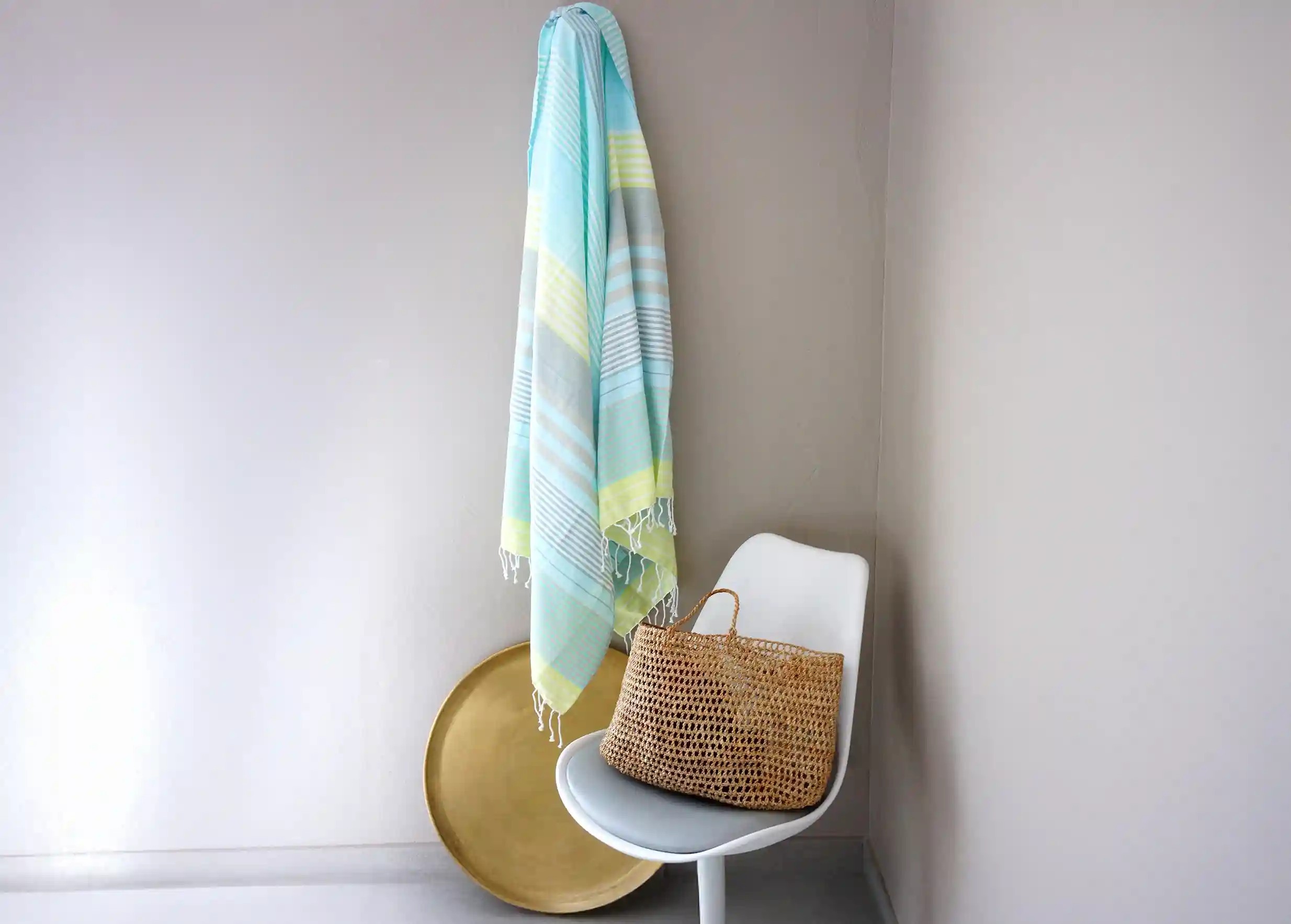 Sunny Lime coloured fouta in  organic cotton, hanging from a white wall, Moon gold brass tray and bag on a chair.