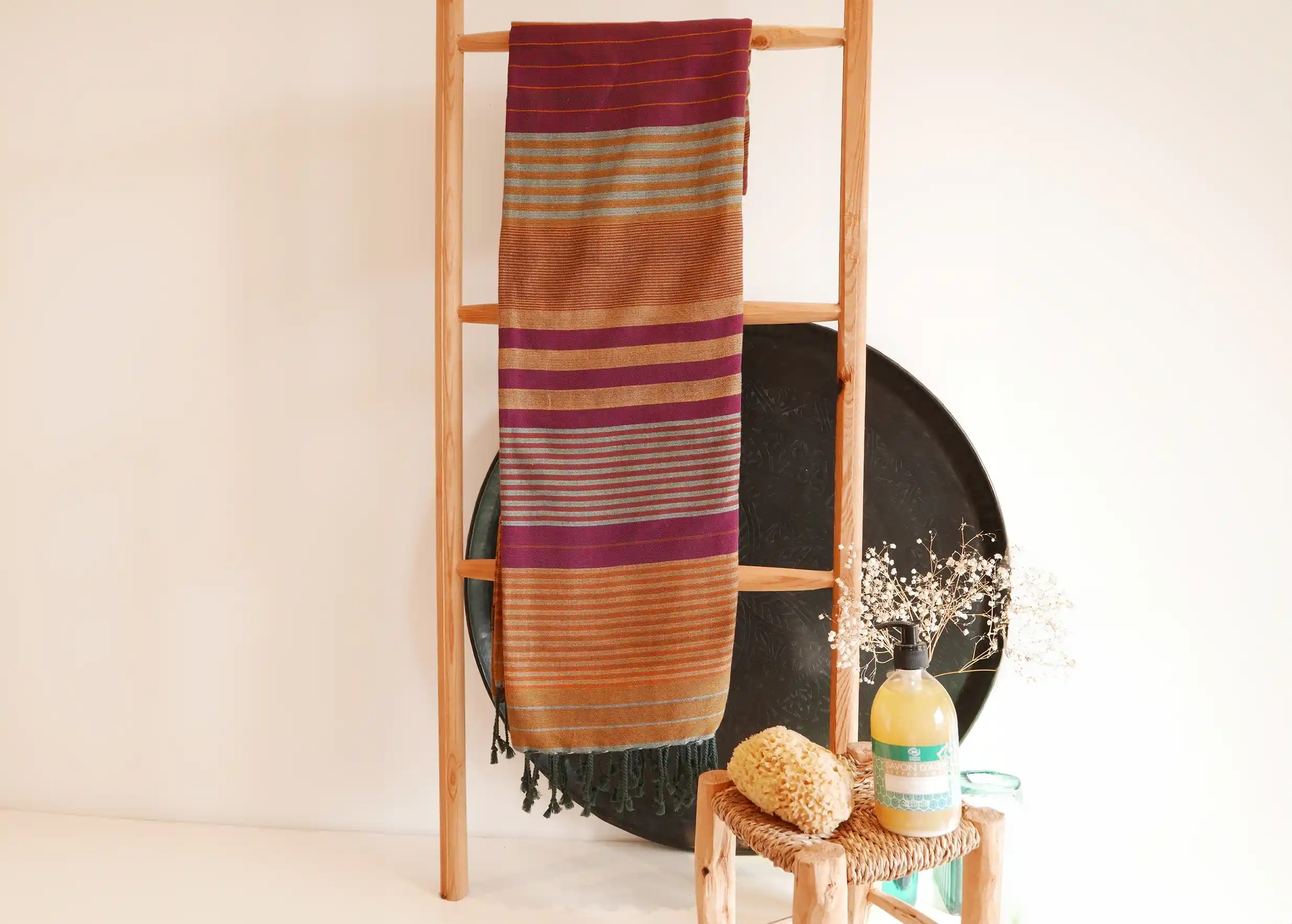 Arabesk-coloured fouta in organic cotton from the Ébène collection on a wooden ladder, brass decorative tray