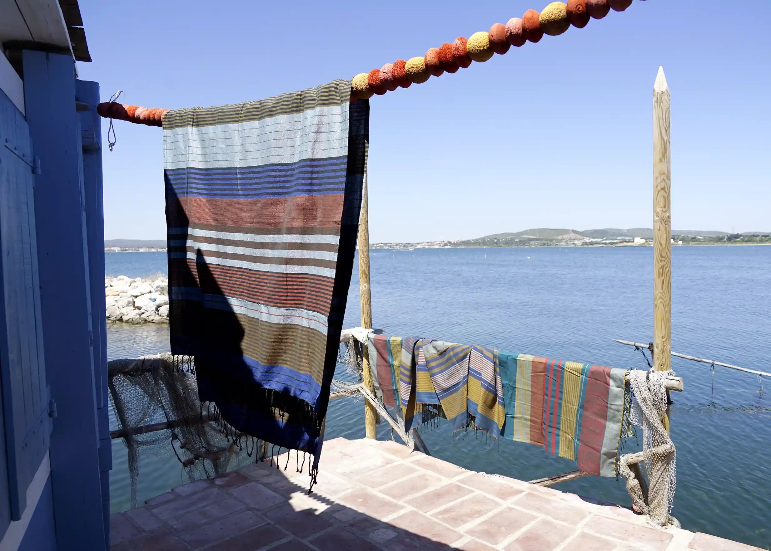 Fouta en coton bio Céleste accrochée en hauteur, décor marin et bateaux en arrière-plan