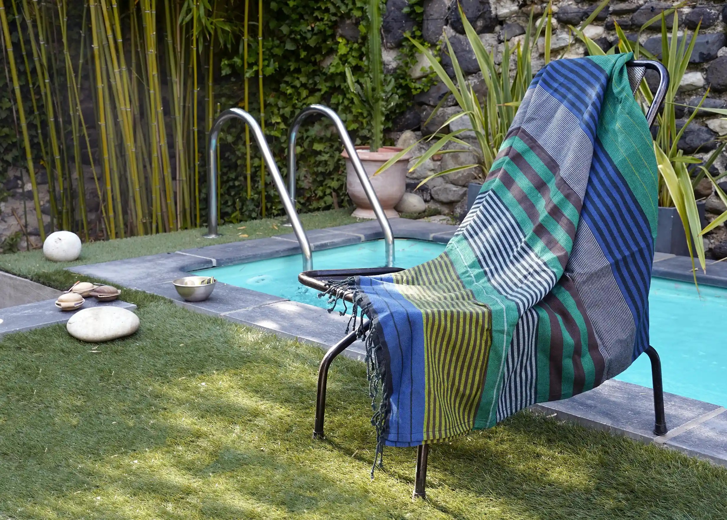 Fouta en coton bio Forest de la collection Ébène par Karawan étendue sur une chaise, près d'une piscine