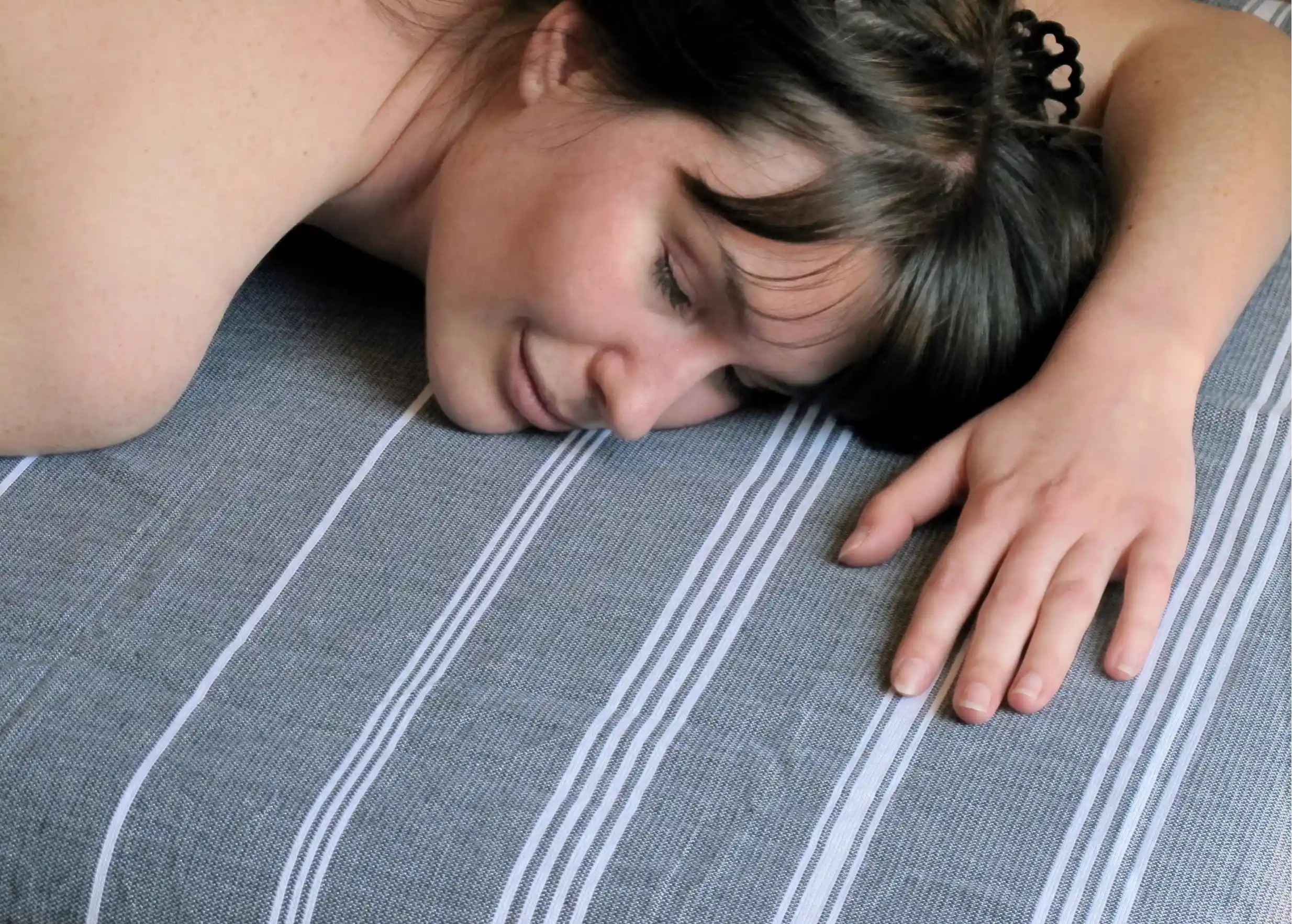 Femme allongée sur fouta en coton bio Hammam tissée avec des rayures blanches et des franges nouées Femme allongée sur fouta en coton bio Hammam tissée avec des rayures blanches et des franges nouées