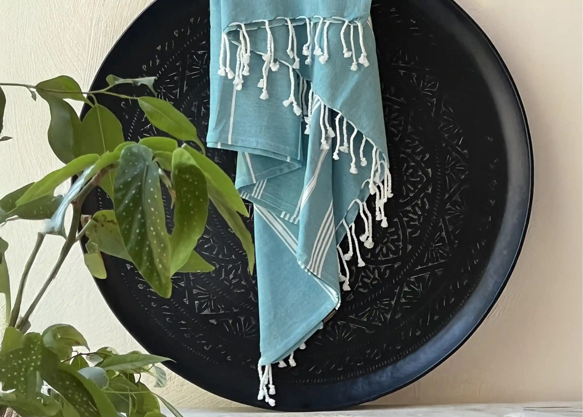 Fouta hammam coloris bleu atoll, posé sur une coupelle en laiton noir, et plante en décoration Fouta hammam coloris bleu atoll, posé sur une coupelle en laiton noir, et plante en décoration