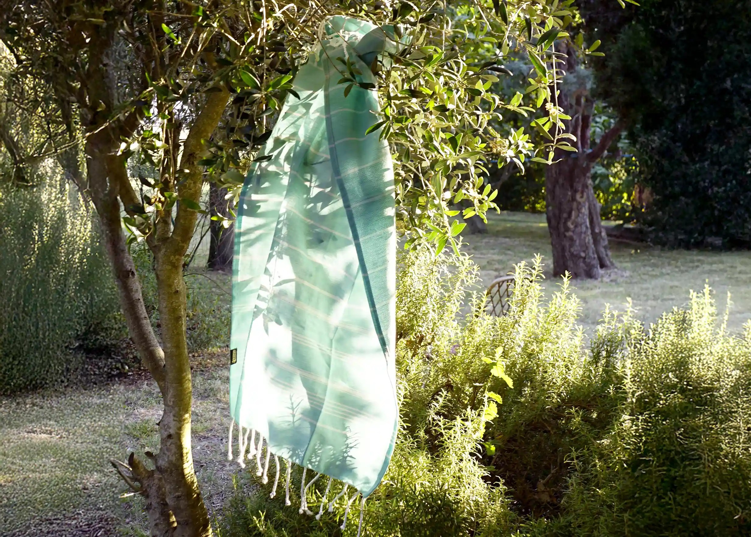 Fouta en coton biologique couleur menthe, accrochée à une branche d'arbre dans un environnement verdoyant et ensoleillé Fouta en coton biologique couleur menthe, accrochée à une branche d'arbre dans un environnement verdoyant et ensoleillé