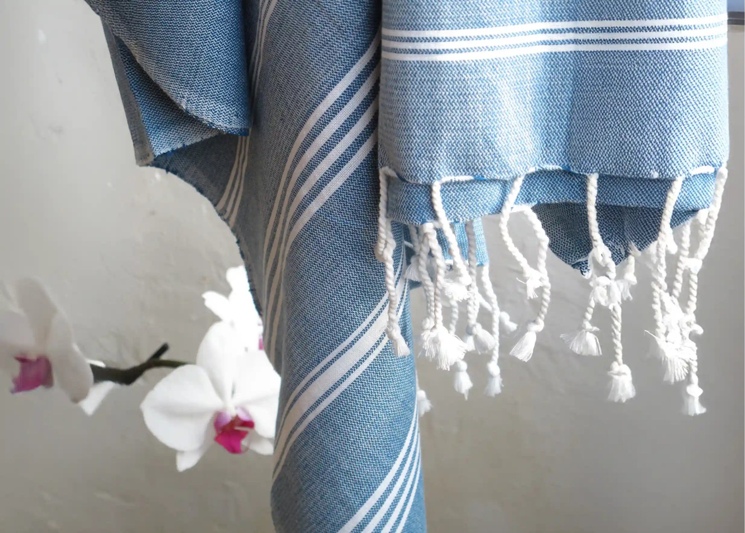 Fouta en coton bio coloris océan vue de près, avec ses rayures blanches et ses franges blanches aux extrémités nouées Fouta en coton bio coloris océan vue de près, avec ses rayures blanches et ses franges blanches aux extrémités nouées
