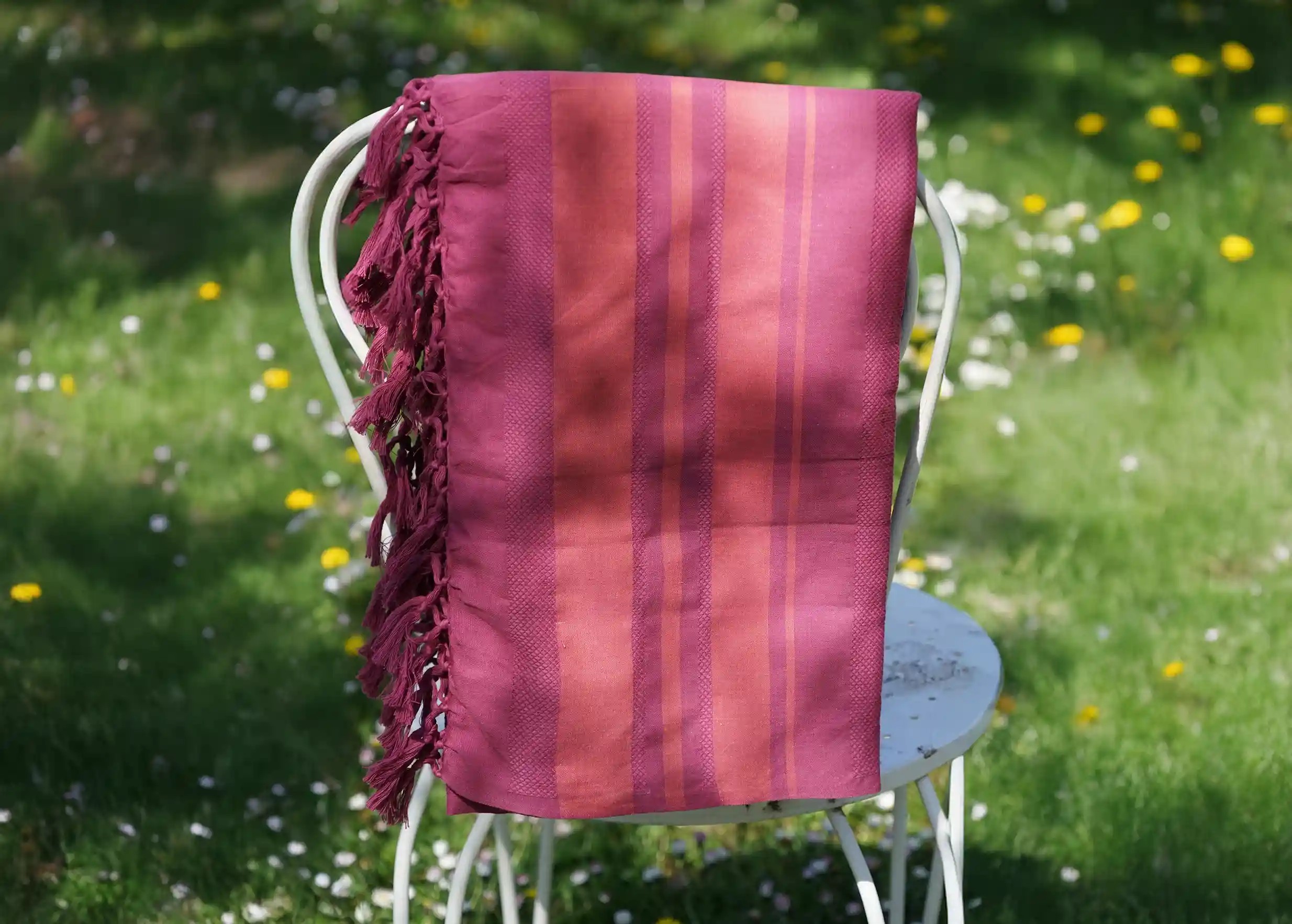 Fouta en coton bio Fushia de la collection Garden, posée sur une chaise,  parterre de fleurs