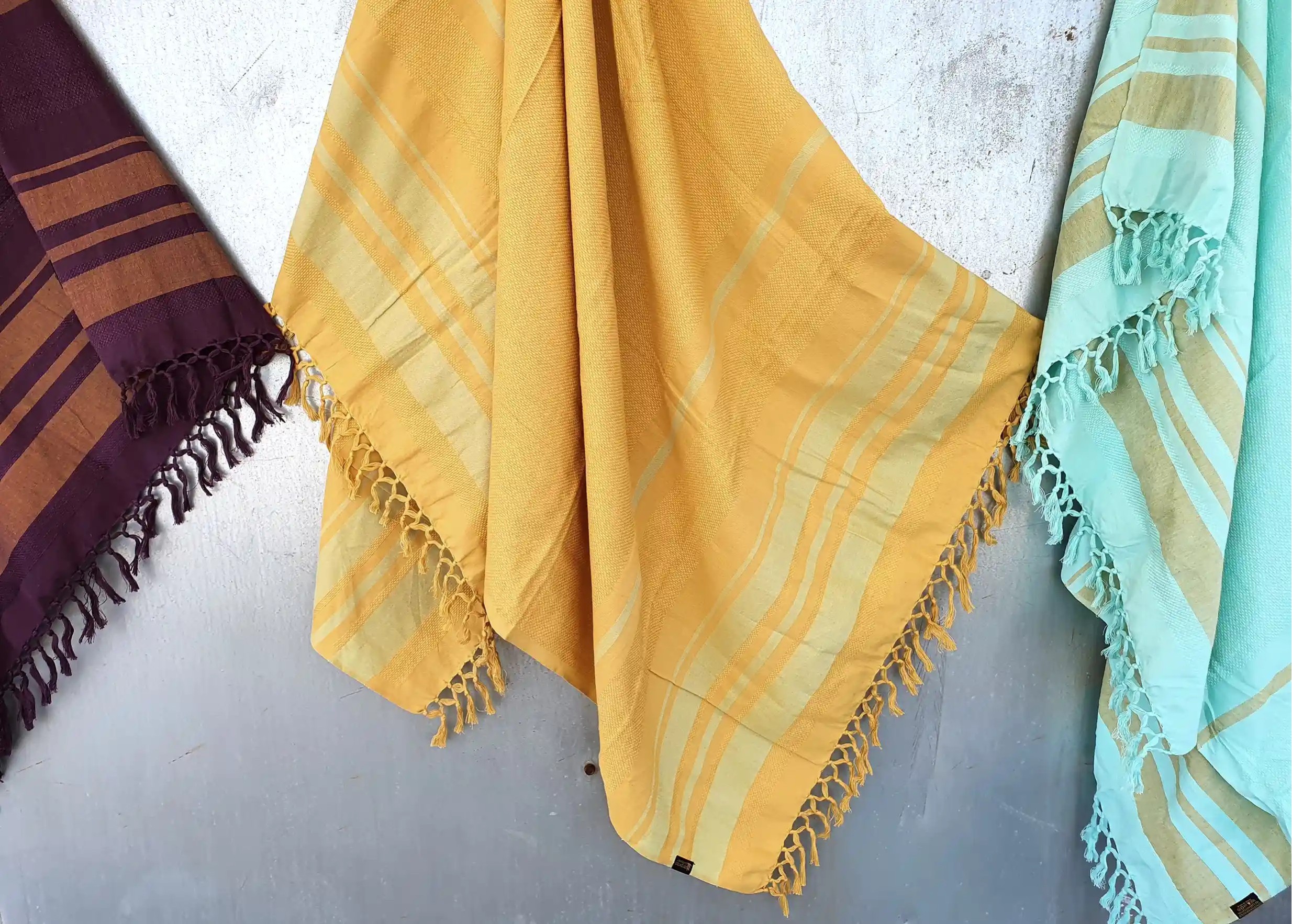 3 Garden organic cotton foutas hung on a wall, in purple, yellow and blue