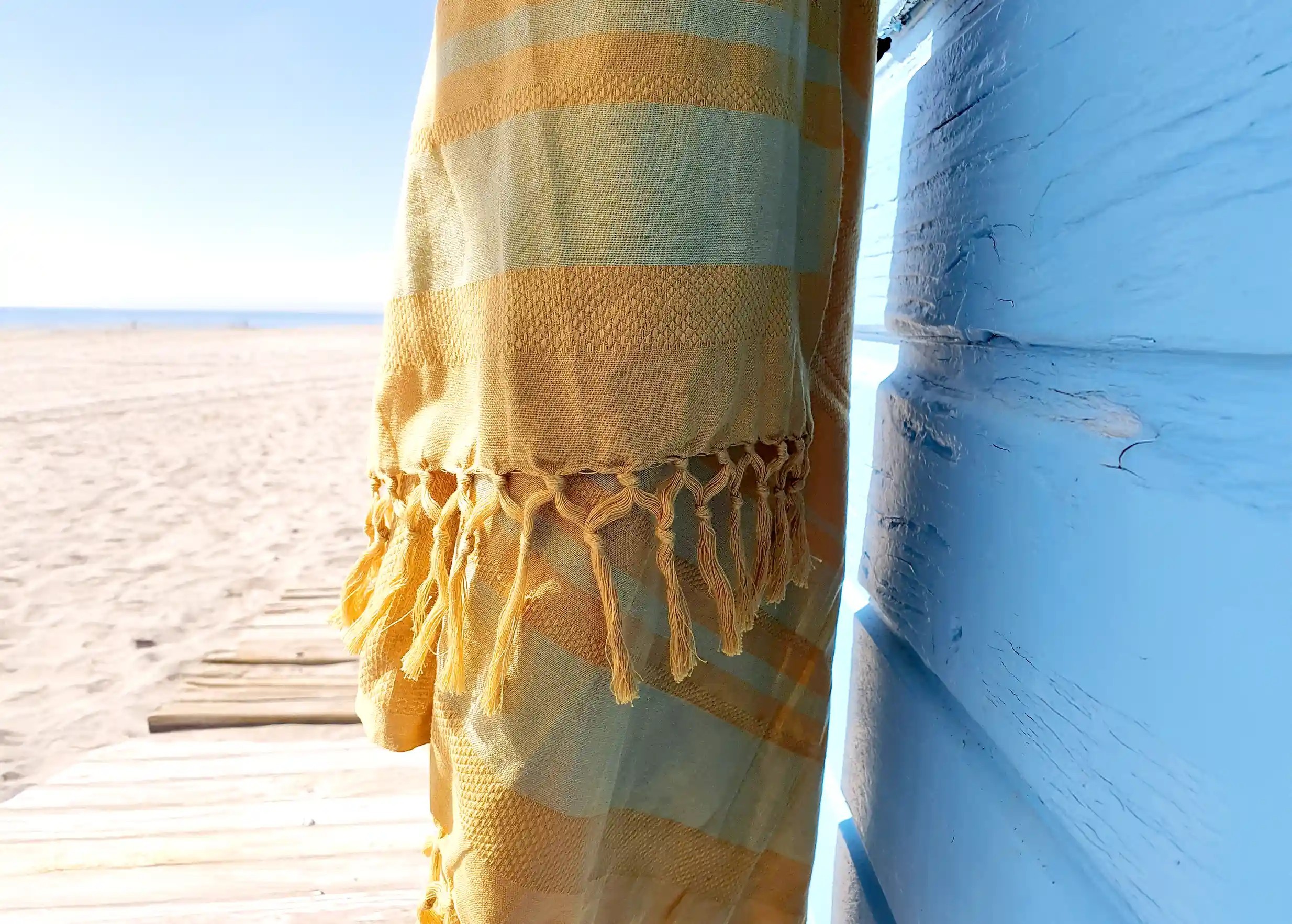 Close-up of sunflower organic cotton fouta with yellow fringes, beach and sea in the distance