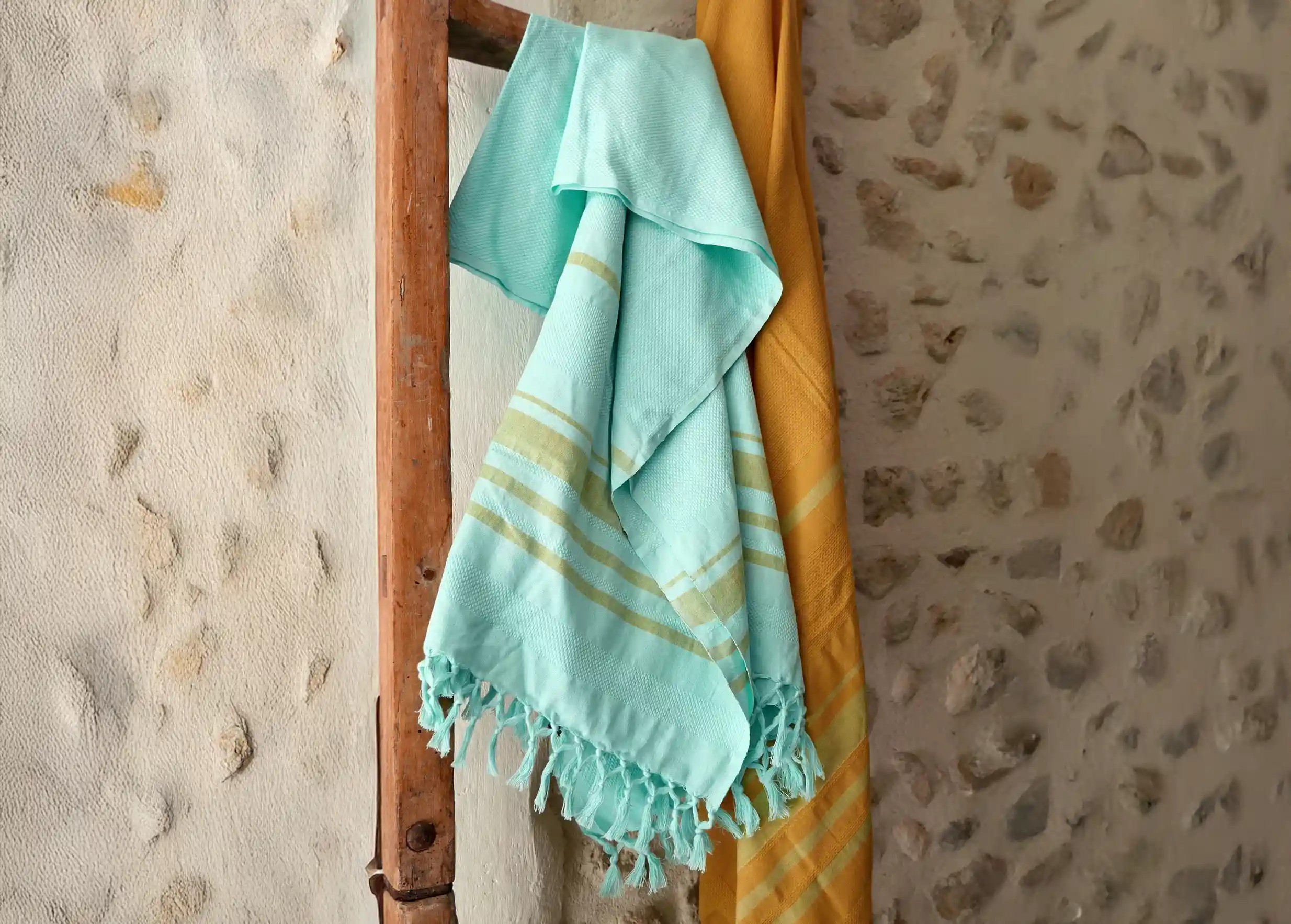 Close-up of the turquoise organic cotton fouta with knotted fringes, placed on a yellow striped fouta.