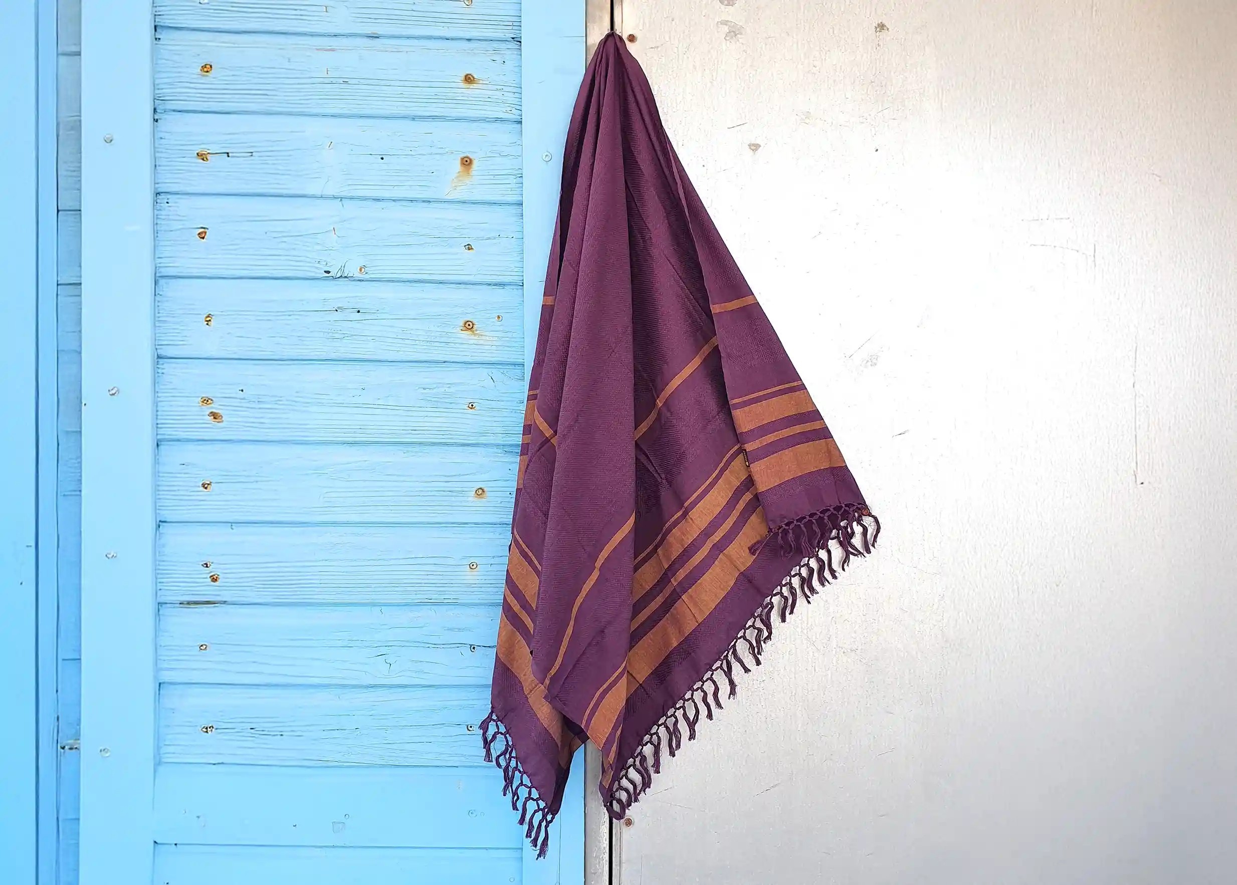Purple-coloured fouta in organic cotton, hung on a wall in front of a light blue background