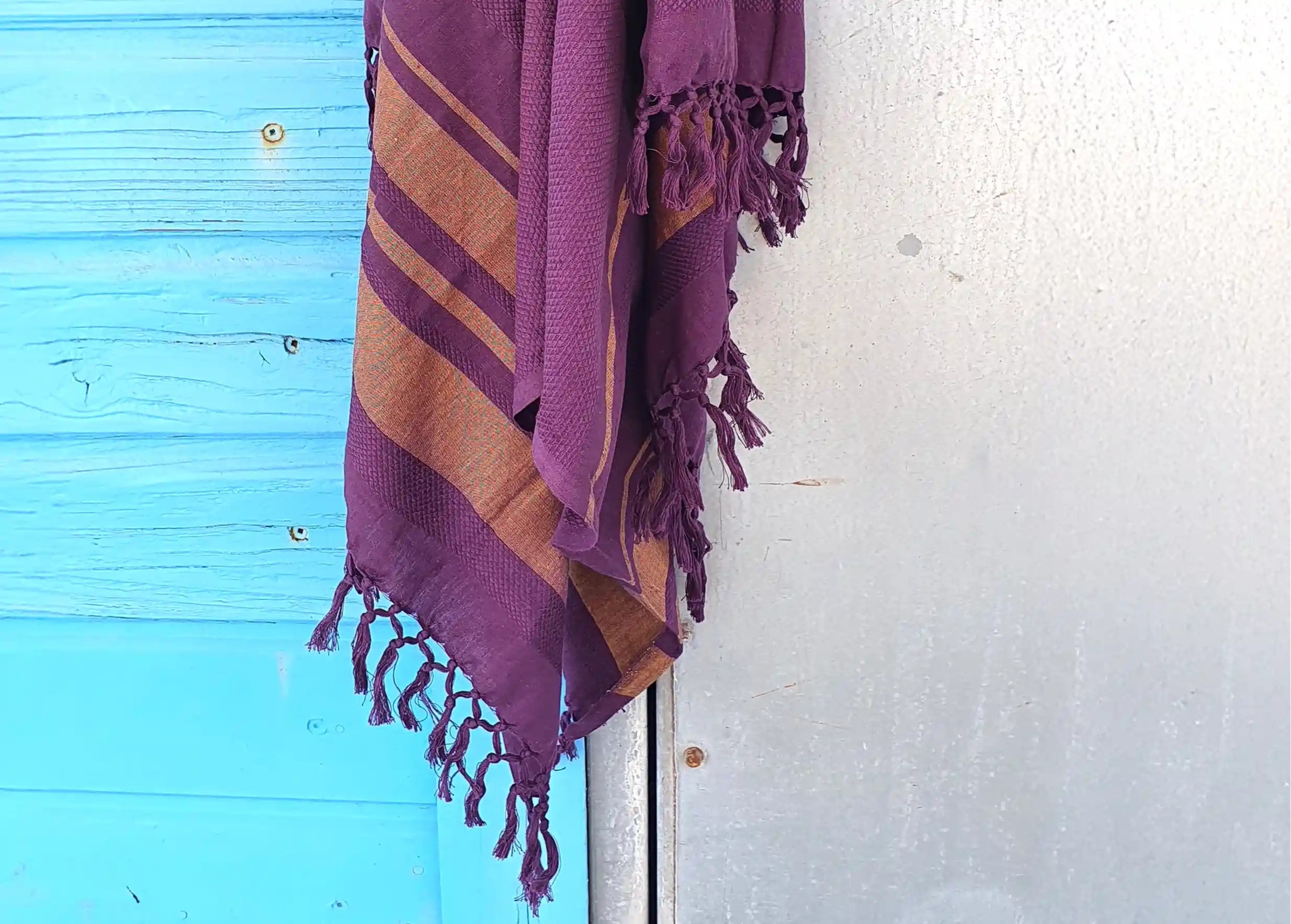 Close-up of the purple-coloured organic cotton fouta with knotted fringes, against a light blue background