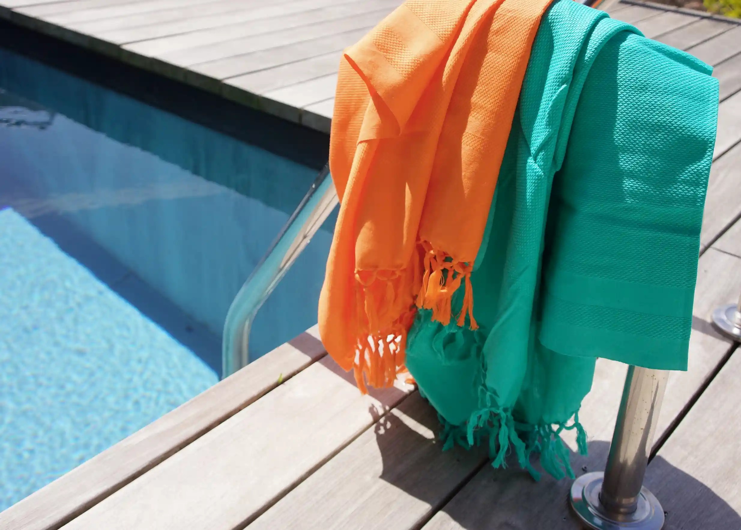 Fouta dhoti Curcuma et fouta dhoti Lagon par Karawan, posées sur une échelle de piscine
