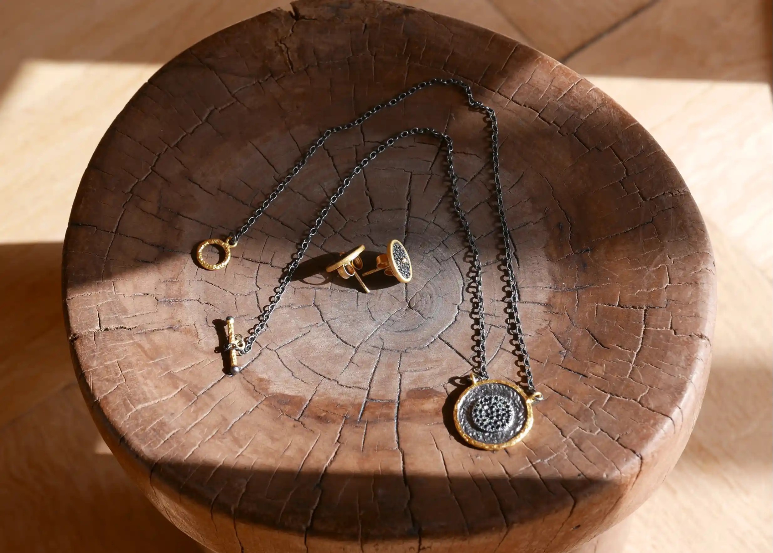 Collection of gilded-plated brass jewellery including bracelets, rings and earrings, presented on a wooden stand.