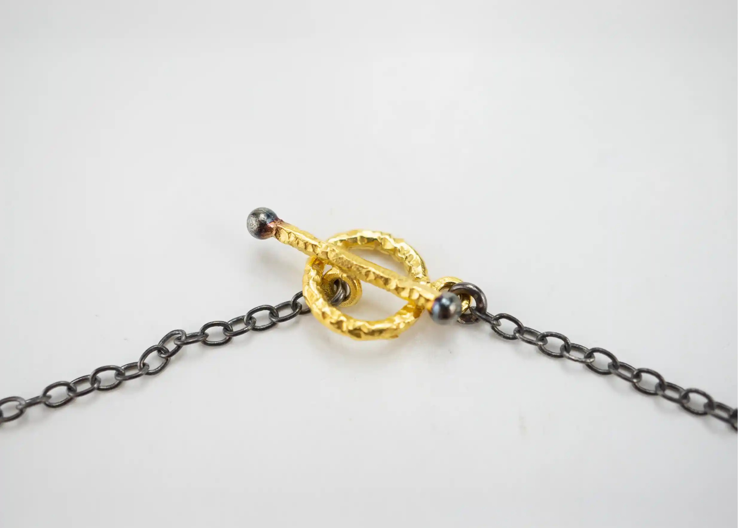 Zoom in on the T-shaped clasp of the gilded-plated brass and zirconium pendant from the Dawn of Time collection