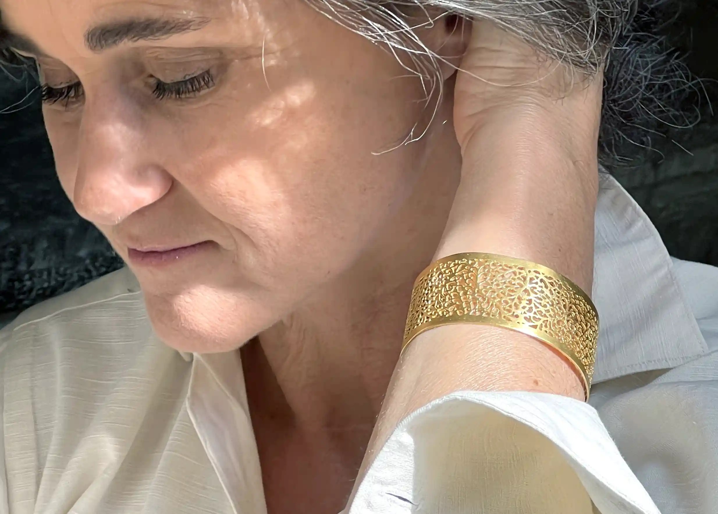 Gilded-plated brass cuff from the Secret Garden collection worn by a woman in a white shirt