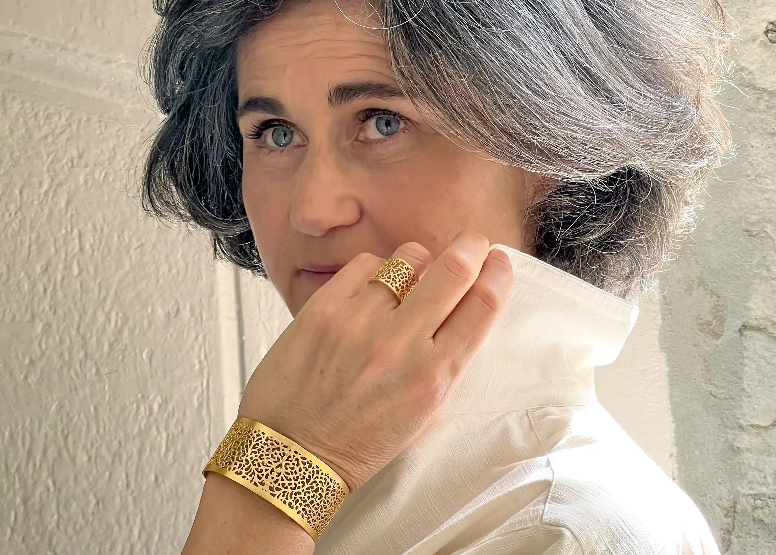 Woman wearing a gilded-plated brass ring from the Secret Garden collection, with a brass cuff and a white top.