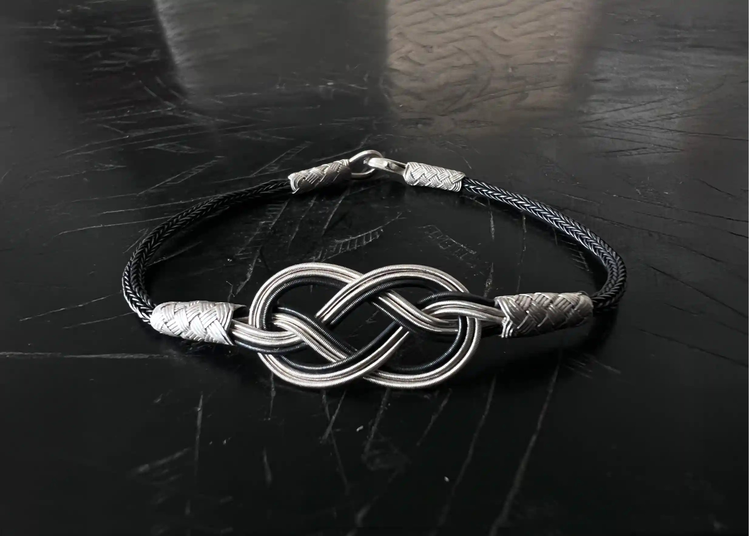 Silver and oxidised silver bracelet from the Kokaz collection, ‘Infinity’ model, set on a black surface
