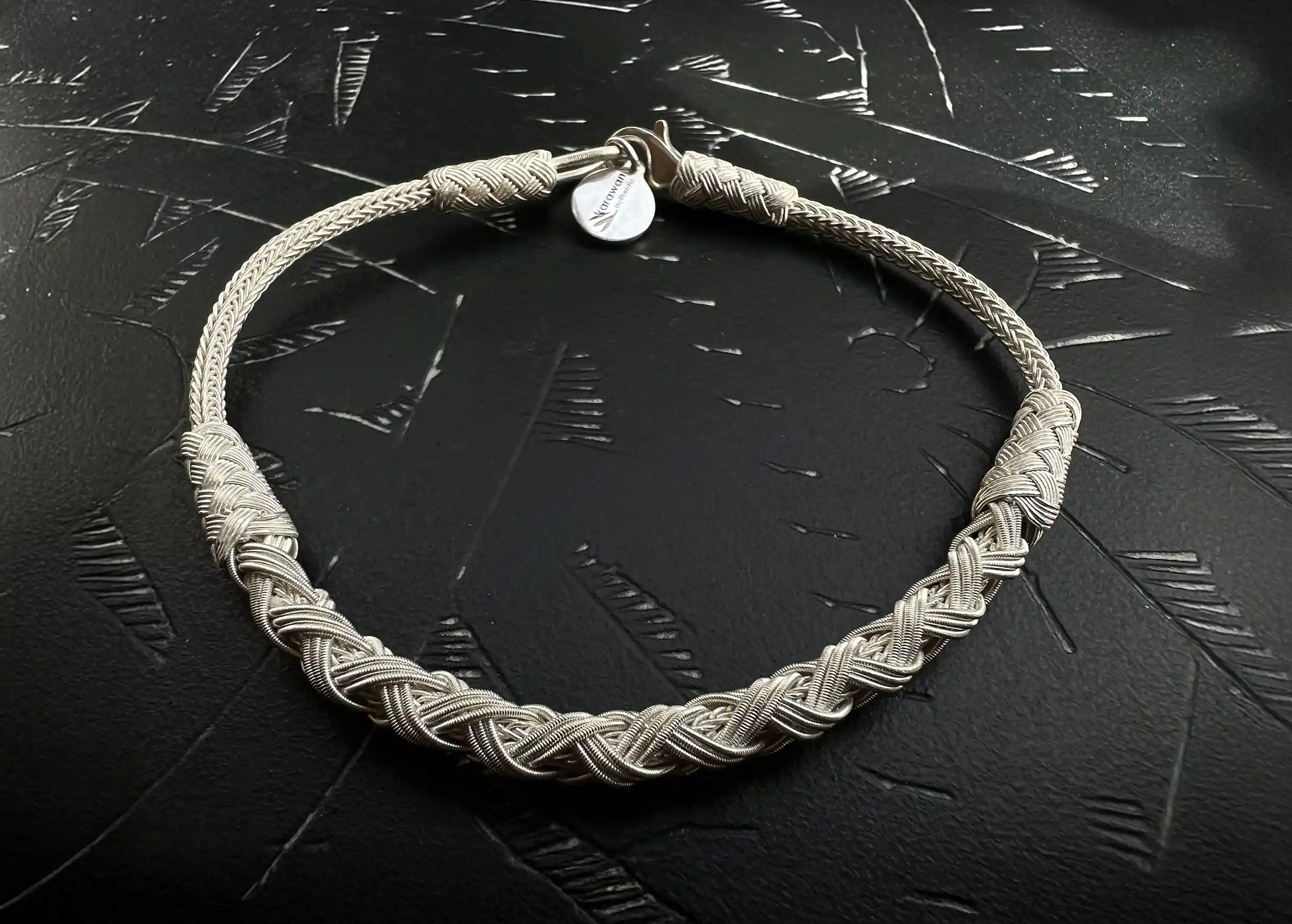 Silver bracelet from the Kokaz jewellery collection Silver braid set on a textured black surface