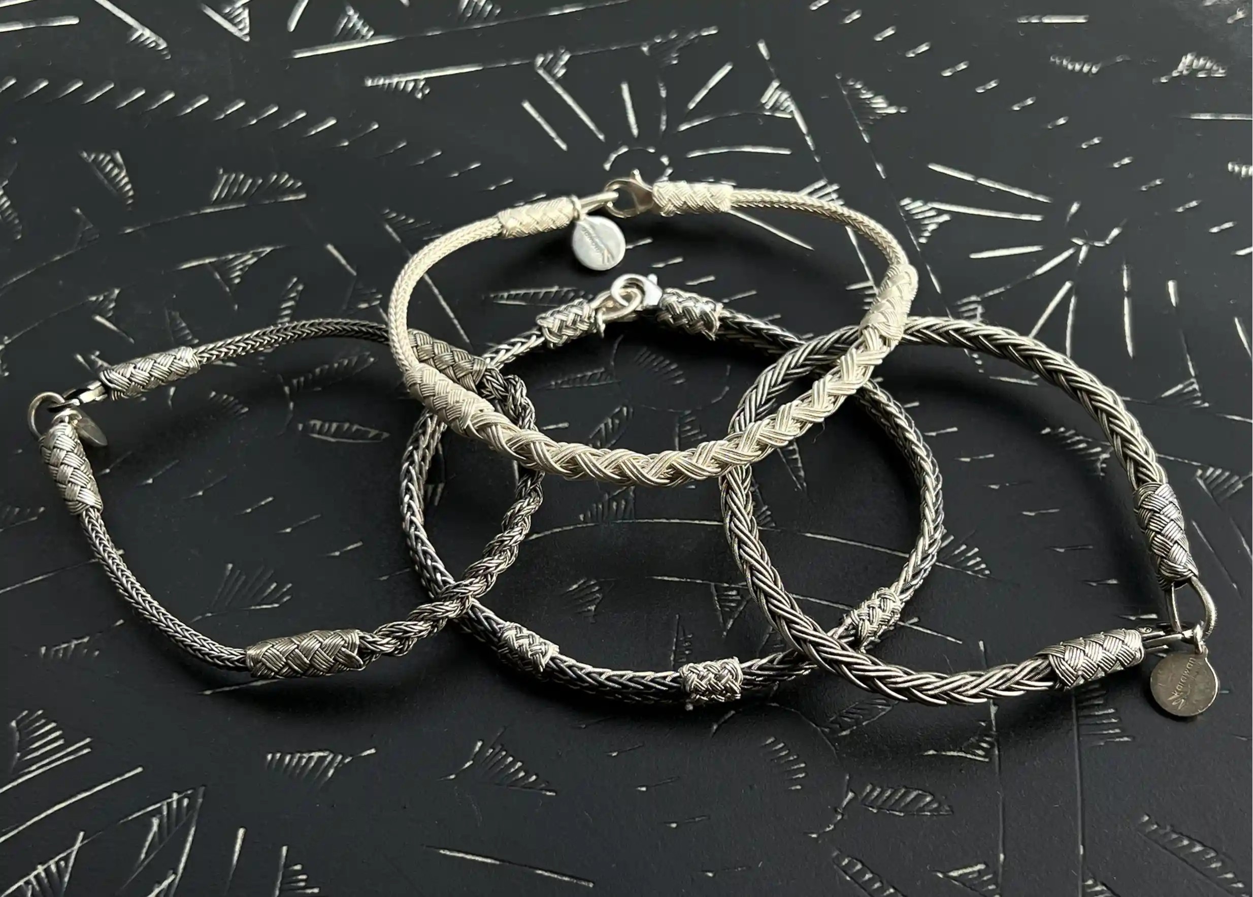 Set of silver bracelets from the Kokaz jewellery collection on a textured black surface