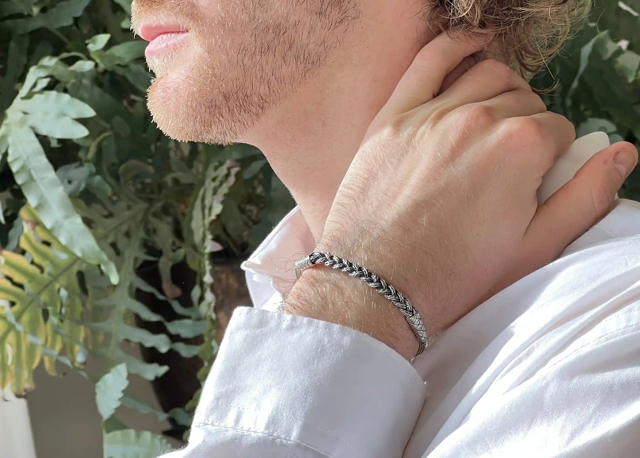 Silver bracelet from the Kokaz jewellery collection, braided chain, worn by a man wearing an indoor white shirt.