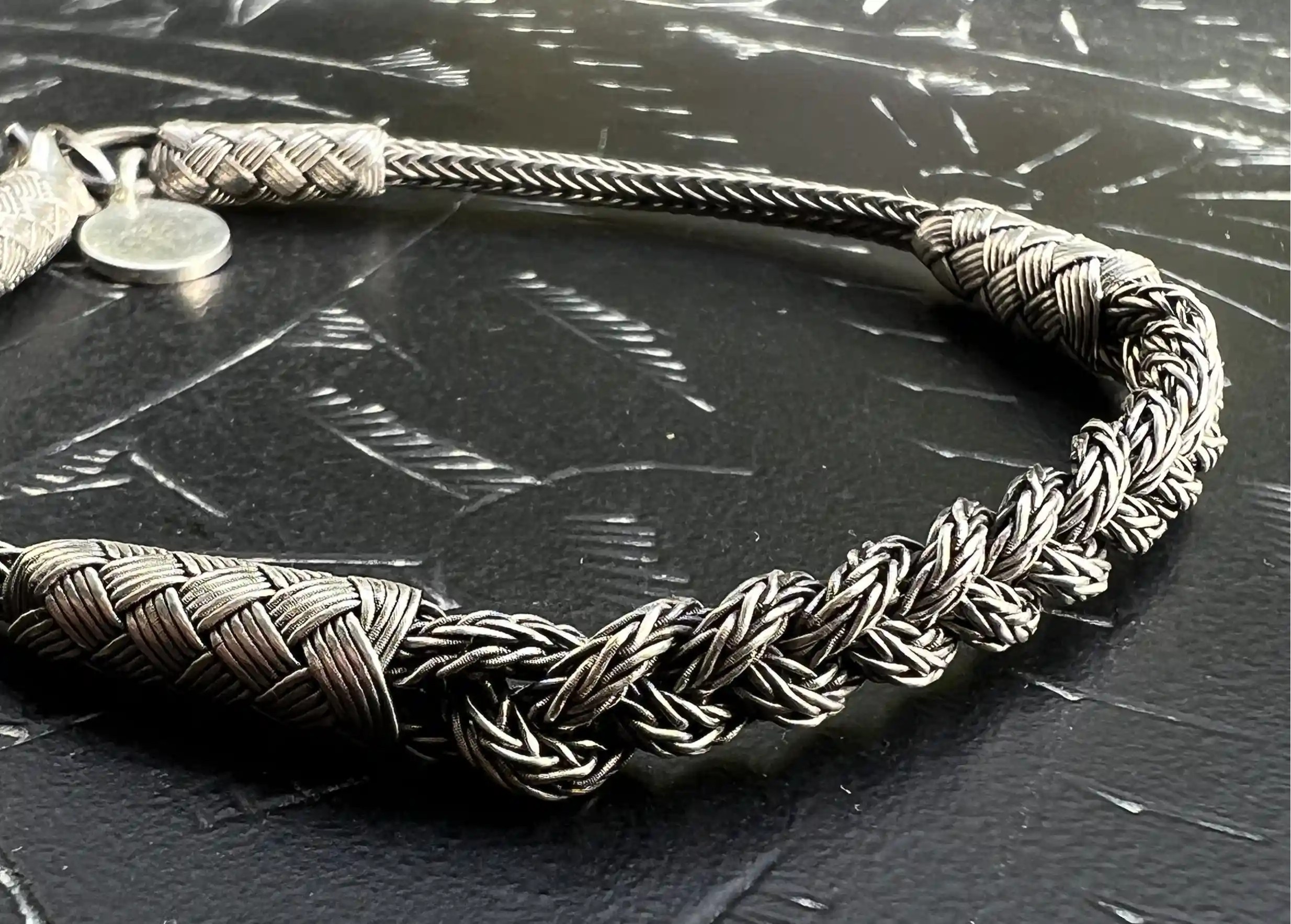 Close-up of a silver bracelet from the Kokaz jewellery collection, braided chain, set on a black surface.