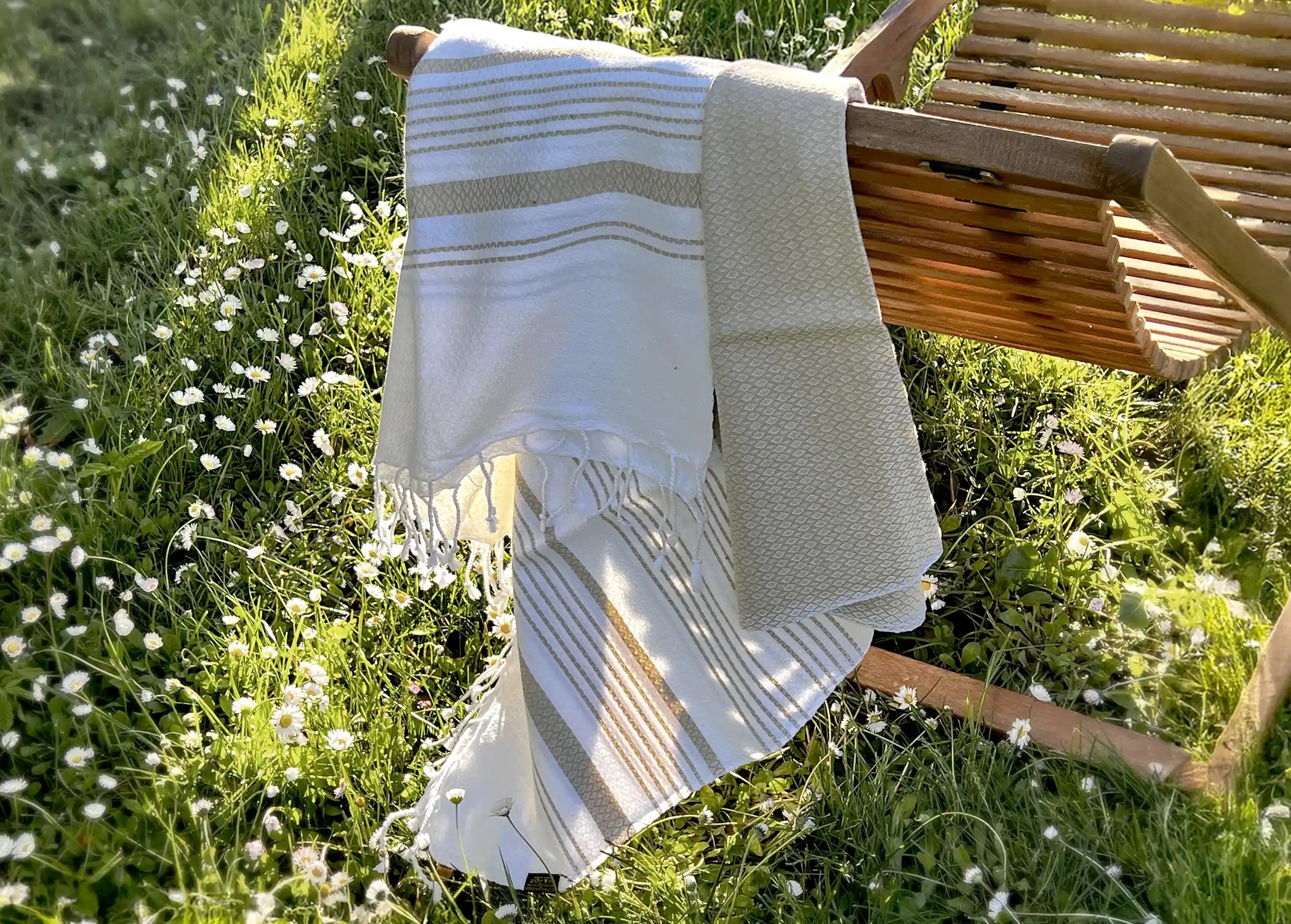 Fouta White Sand, coloris Ginger, tissée sur chaîne blanche et suspendue sur une chaise de jardin