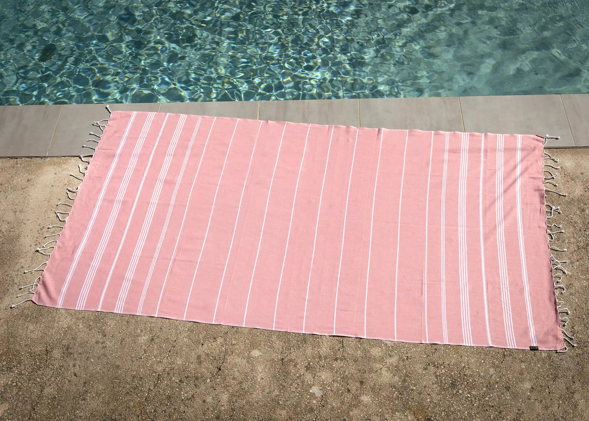 Fouta en coton bio corail, rose et blanche, posée près d'une piscine Fouta en coton bio corail, rose et blanche, posée près d'une piscine
