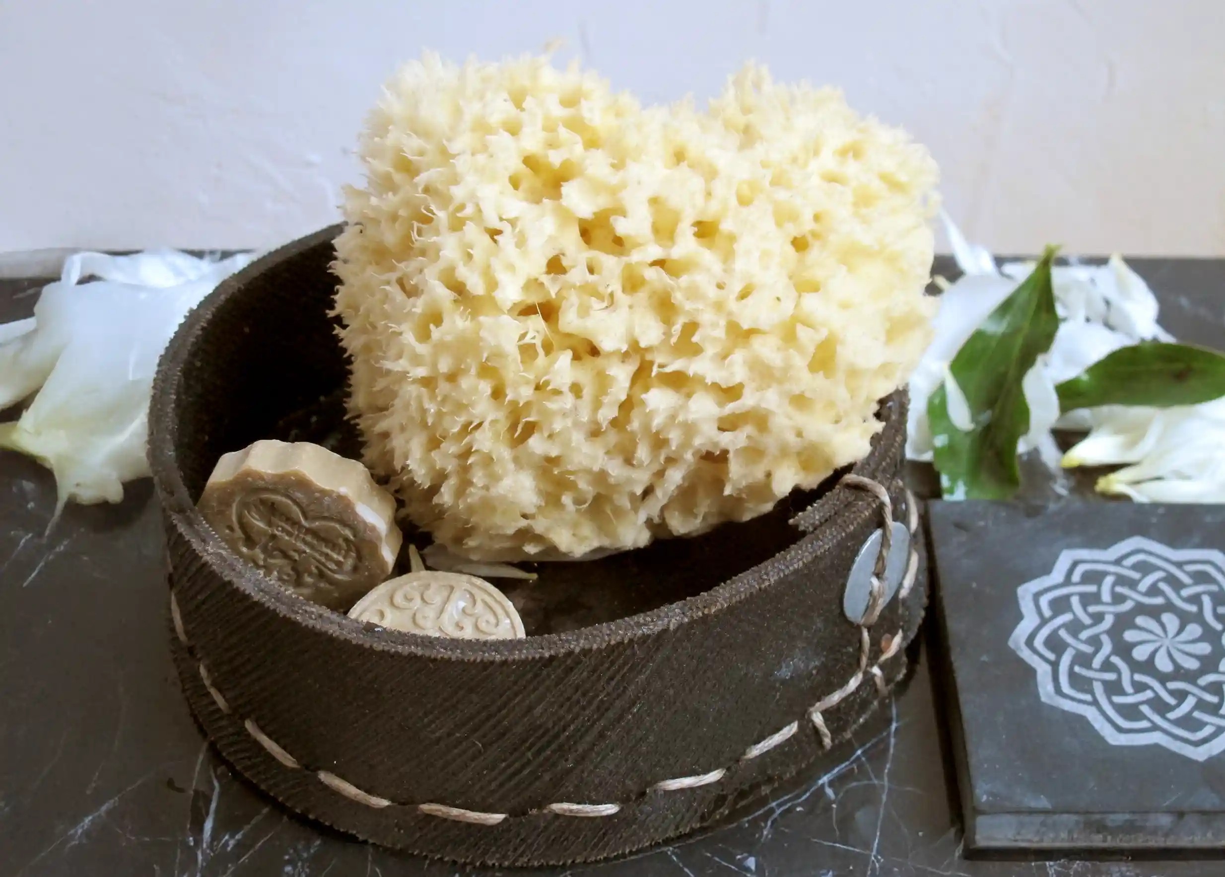 Round pouch in recycled tyres containing a natural sponge and Aleppo soaps, hand-stitched seams and Karawan button