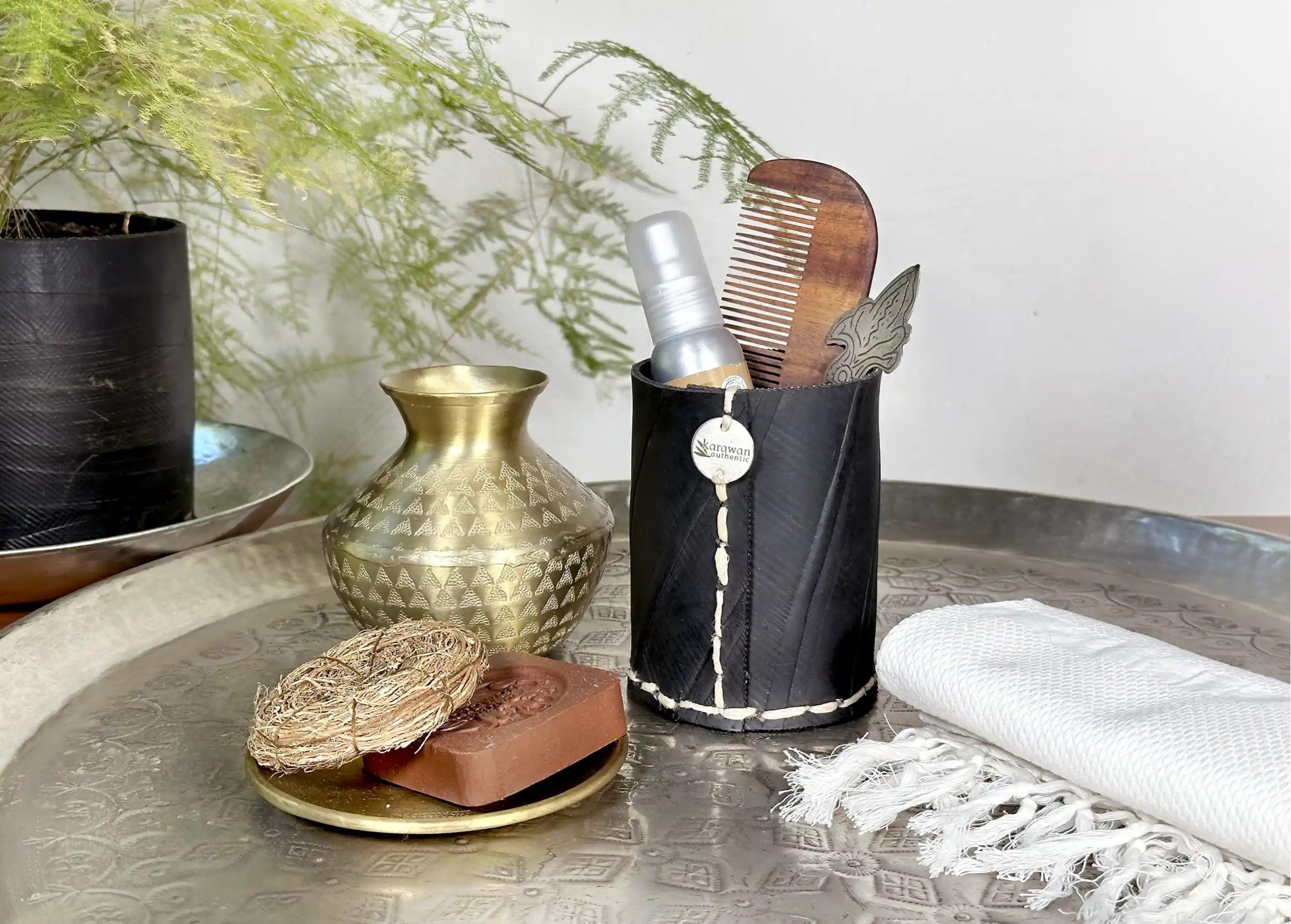 Petit pot droit en pneu recyclé noir avec couture apparente, à côté d'une fouta blanche et d'un vase en aluminium
