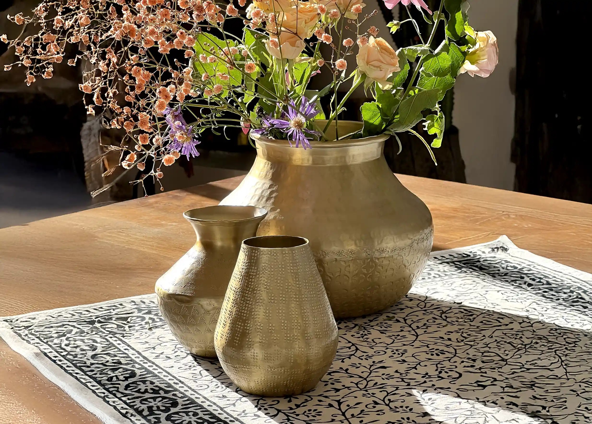 Petit vase déco en aluminium recyclé, finition dorée mate martelée et des motifs gravés, l'ombre des fleurs projetée sur le mur