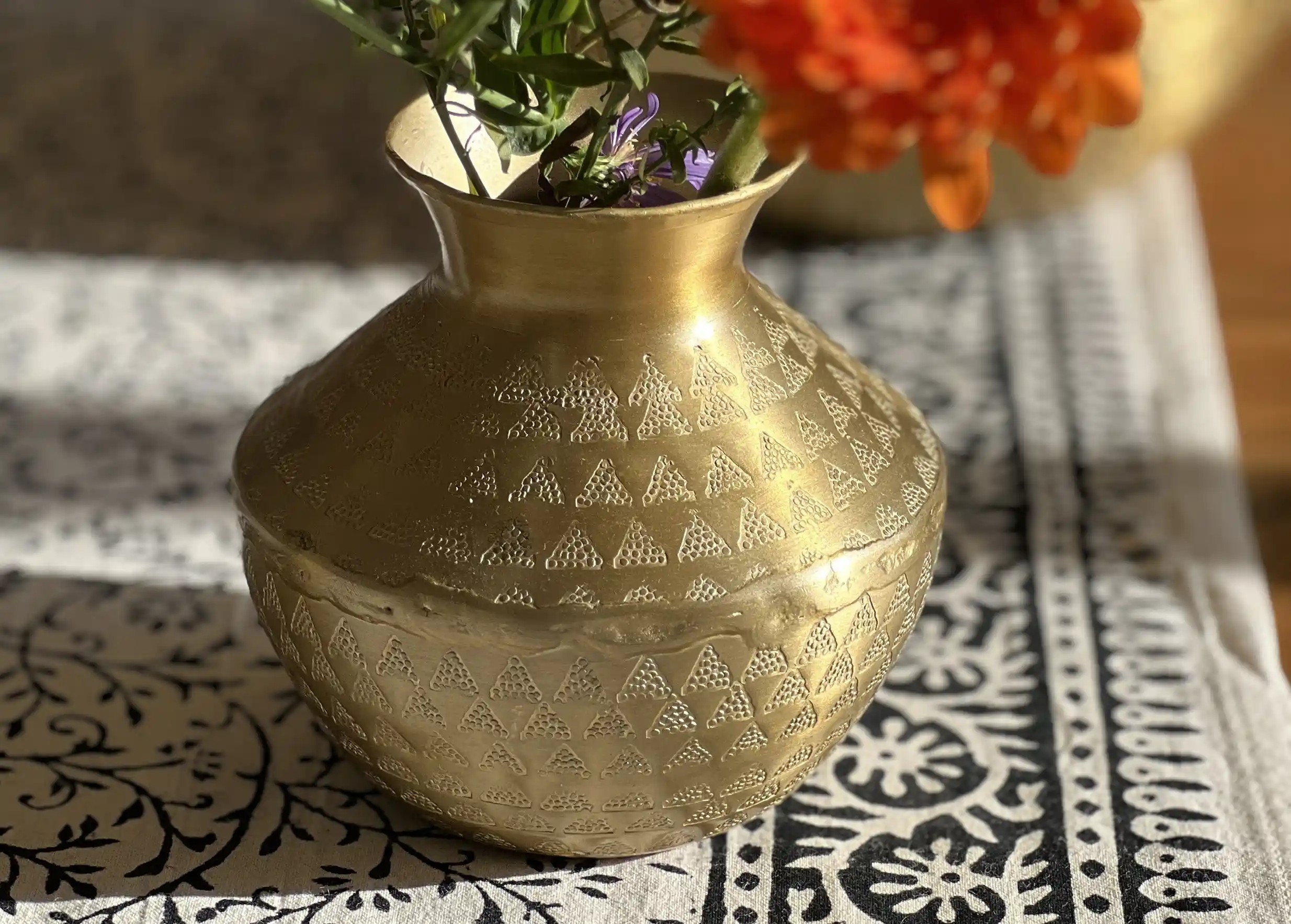 Vase déco en alu recyclé,  coloris doré mat avec une finition martelée, contenant un bouquet de fleurs colorées, sur un napperon