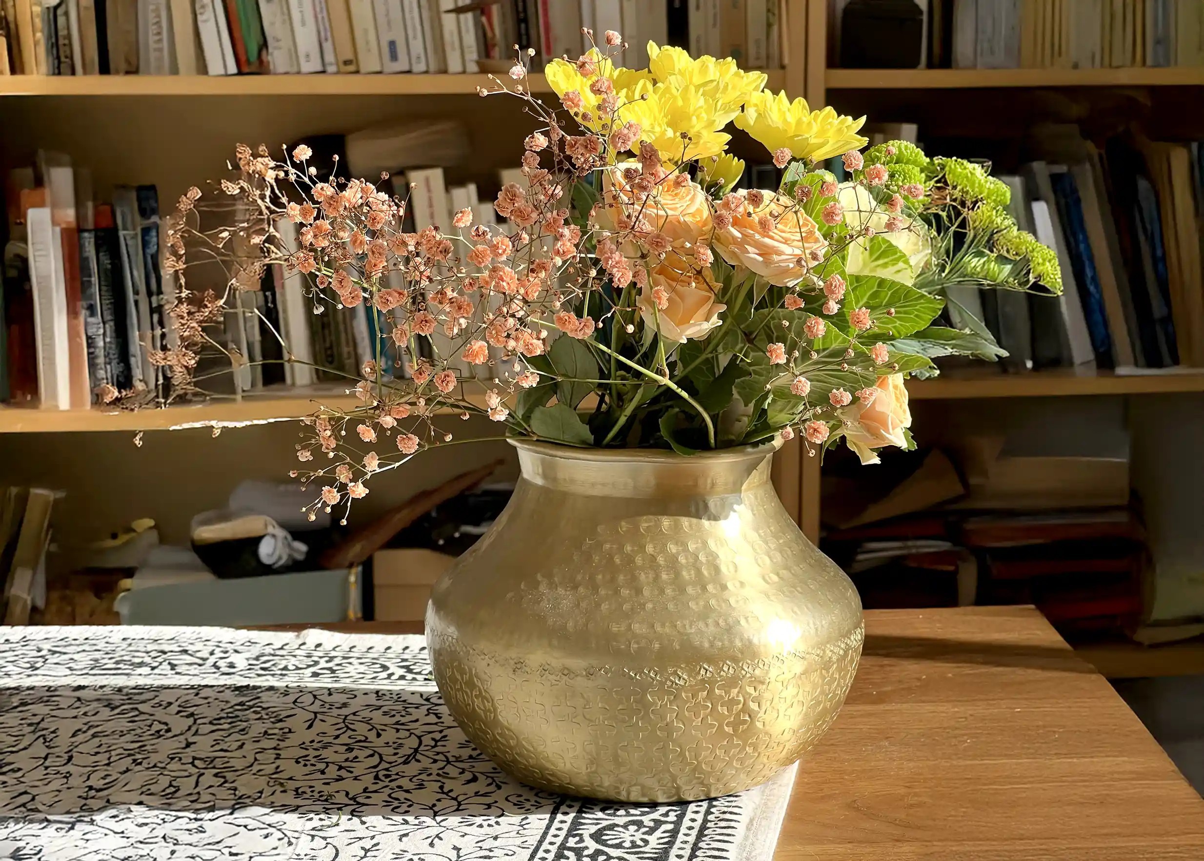 Grand vase déco au coloris doré mat, à la finition martelée, garni de fleurs, bibliothèque en arrière-plan