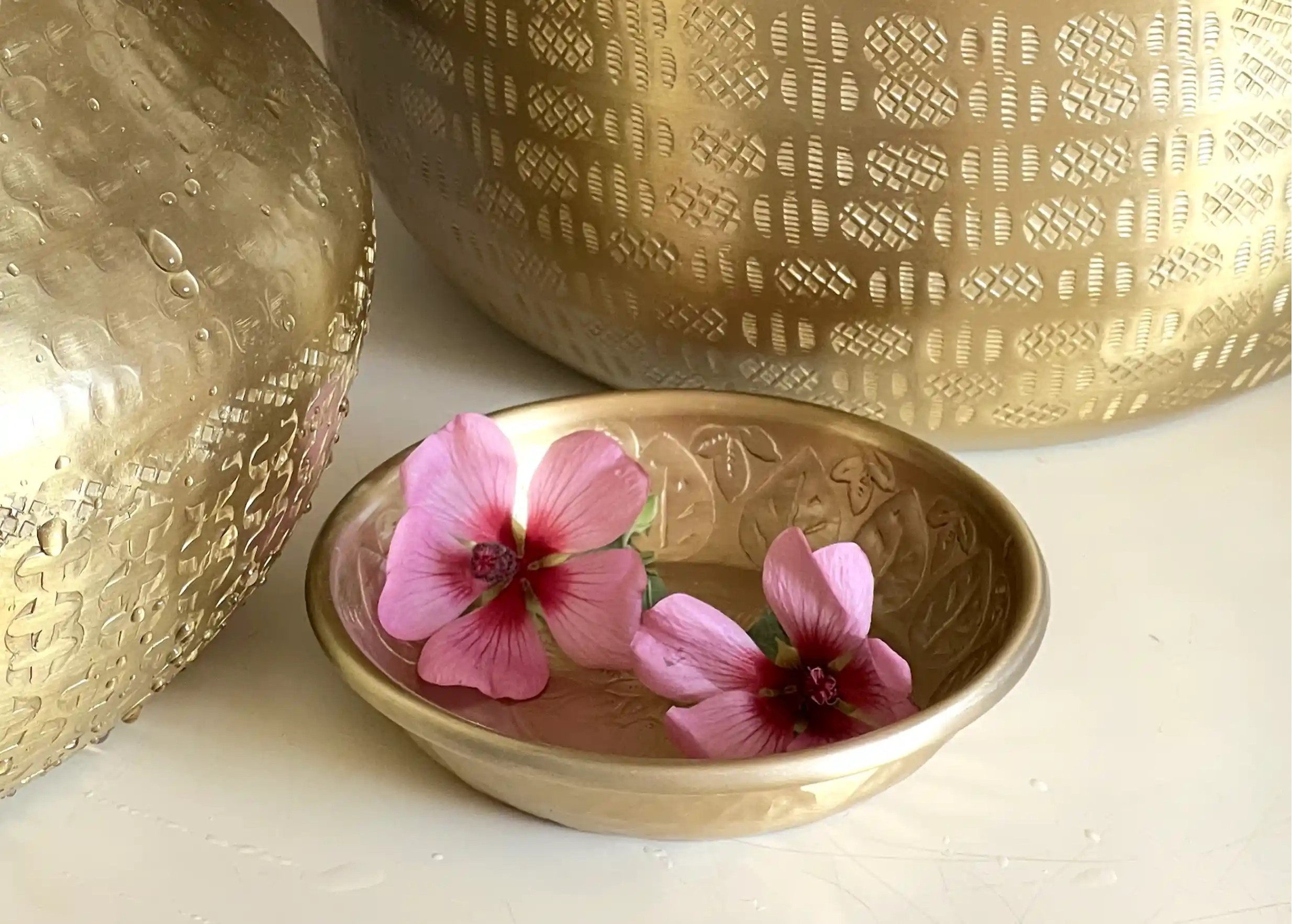 Coupelle en aluminium doré avec une finition gravée, contenant deux fleurs roses, vases gravés en alu à proximité