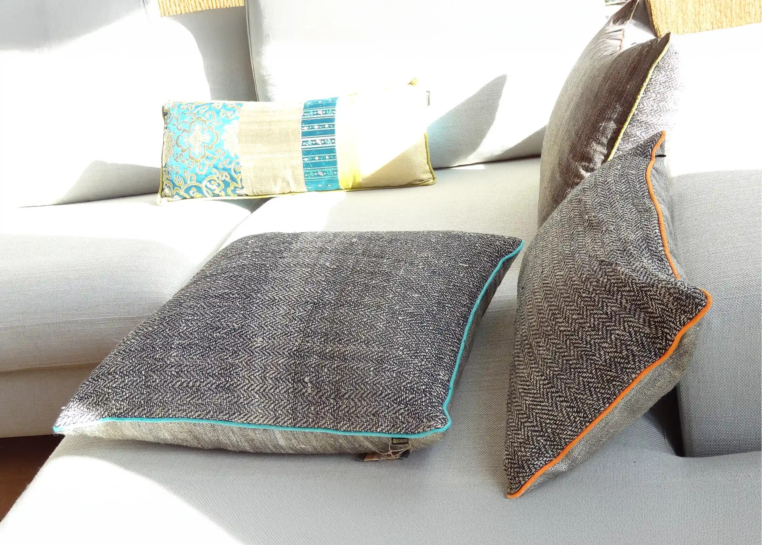 3 large decorative cushions made from nettle fiber and wild silk, with a book in the background placed on a sofa