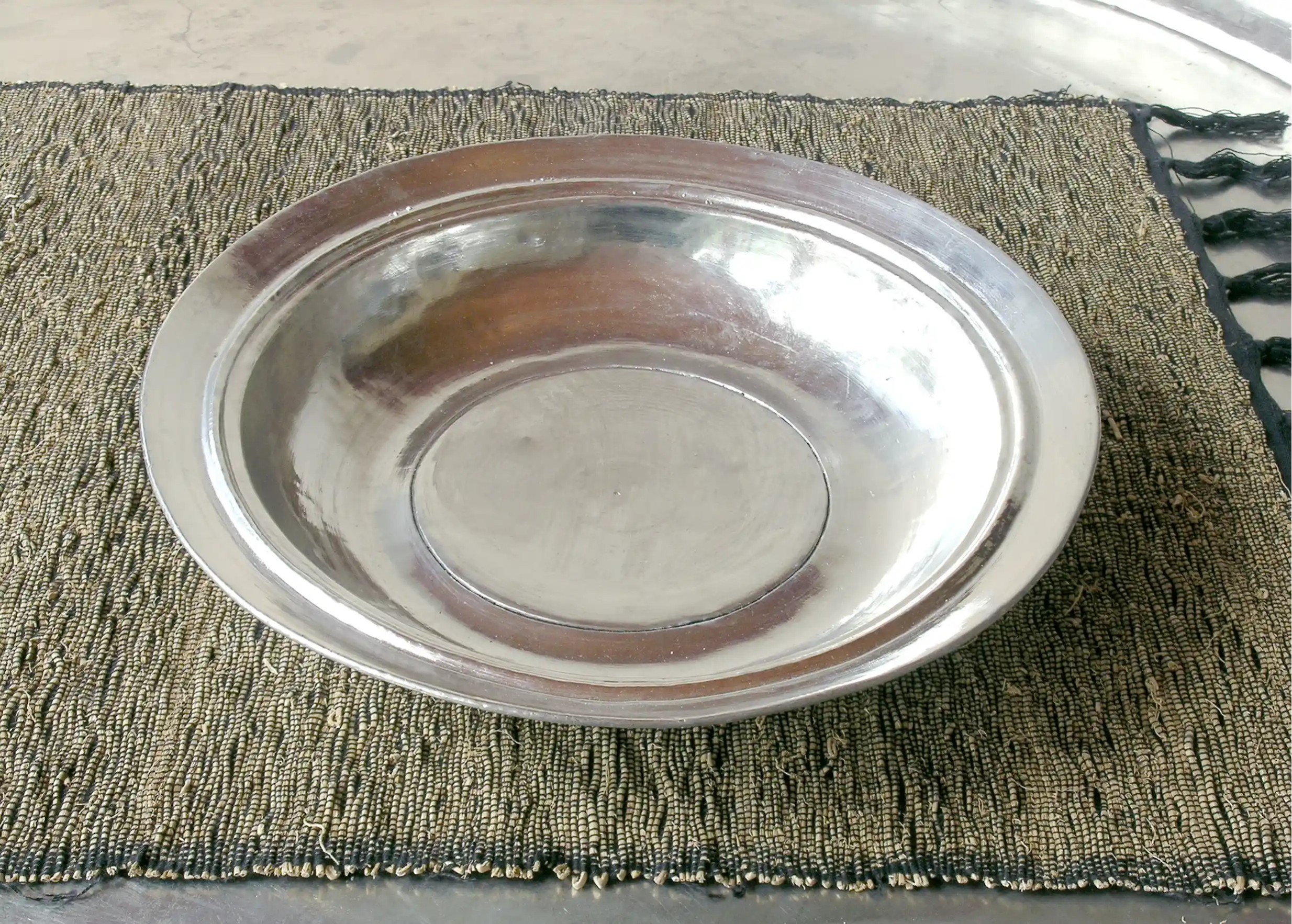 Assiette creuse ancienne en cuivre étamé, posée sur un tissu texturé de couleur foncée