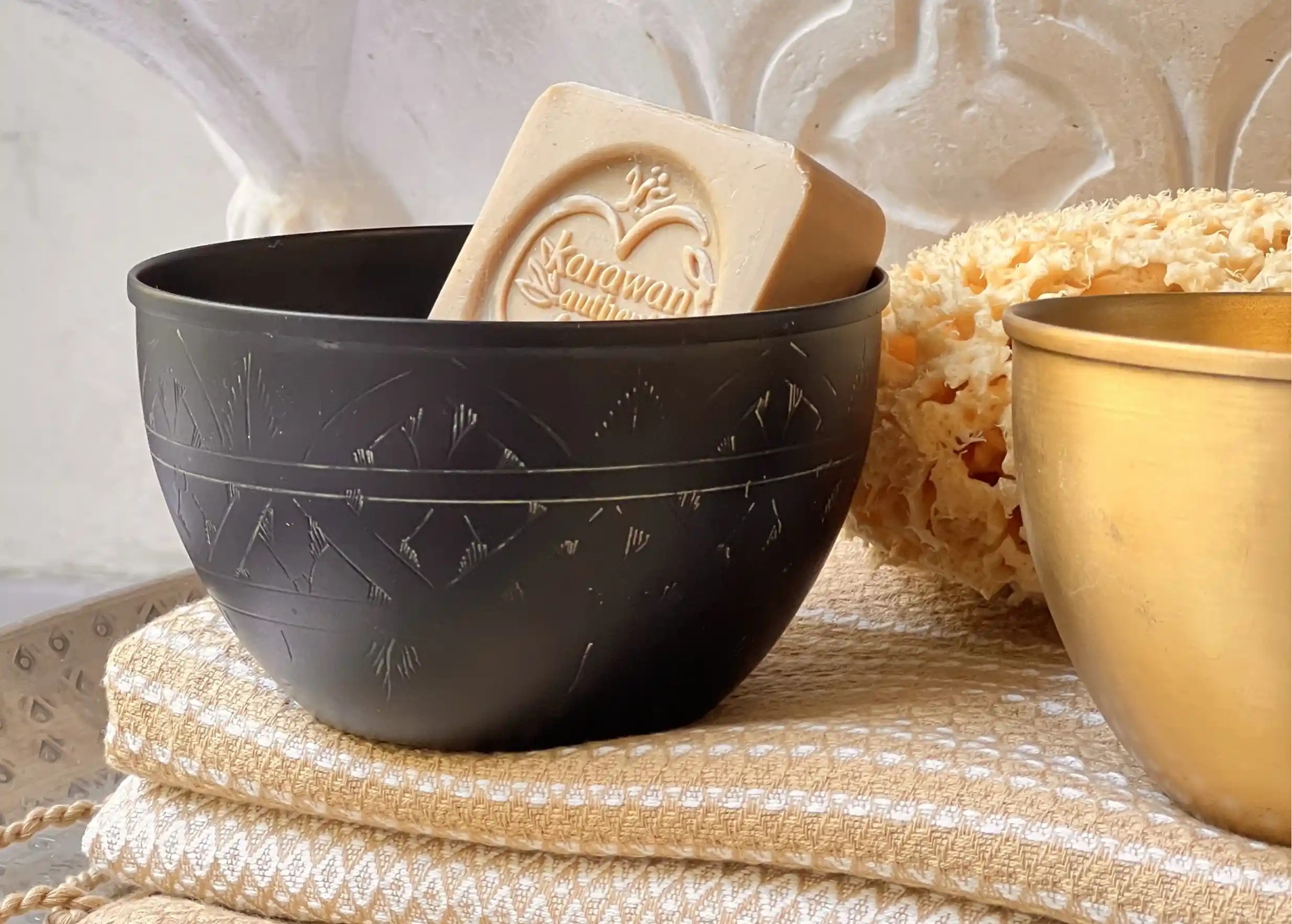 Bol en laiton noir contenant un savon d'Alep, accompagné d'un bol en laiton doré, et un éponge de mer