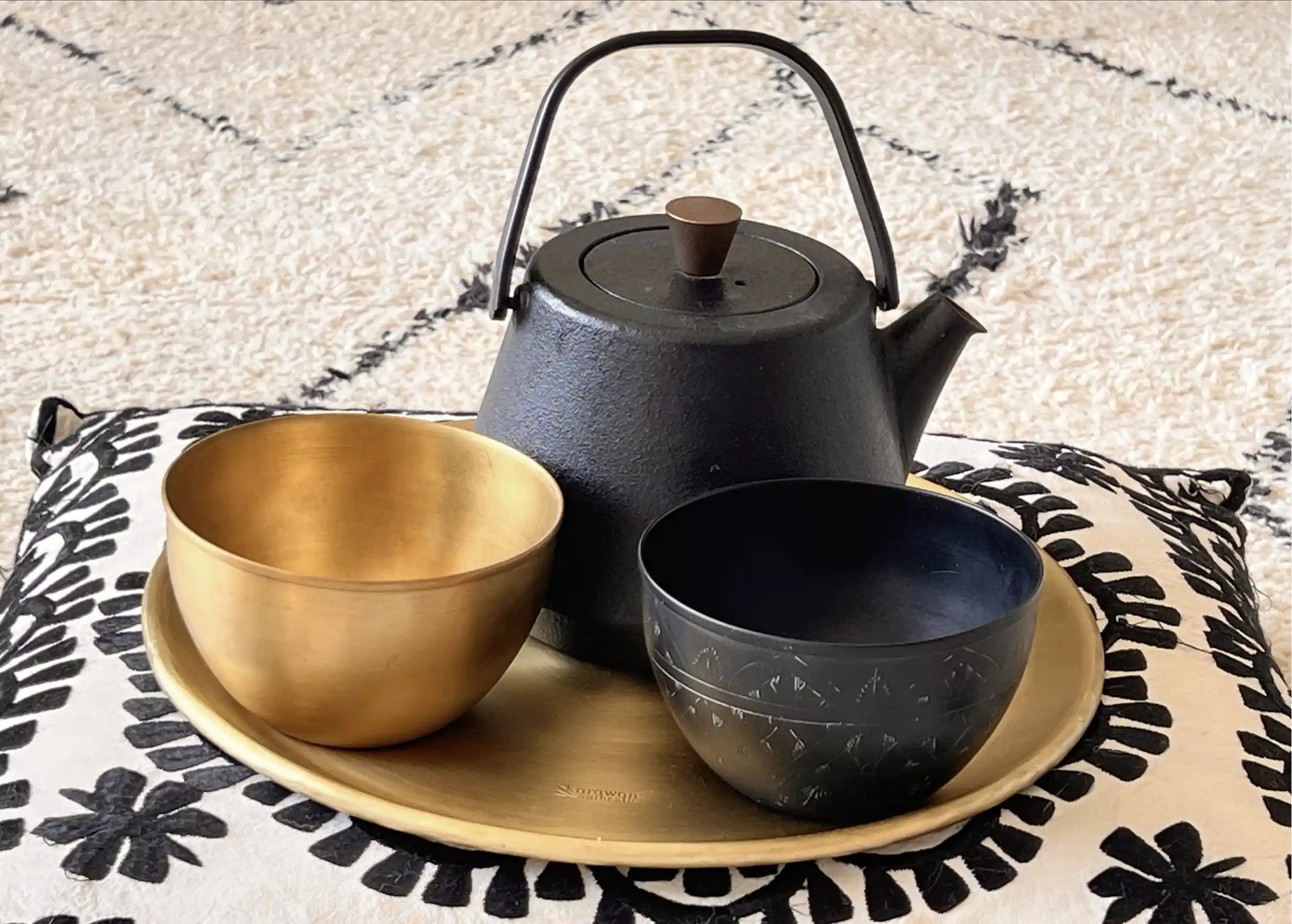 Smooth gold-plated brass bowl, accompanied by a black brass bowl, a black teapot and a gold-plated tray, all on a cushion