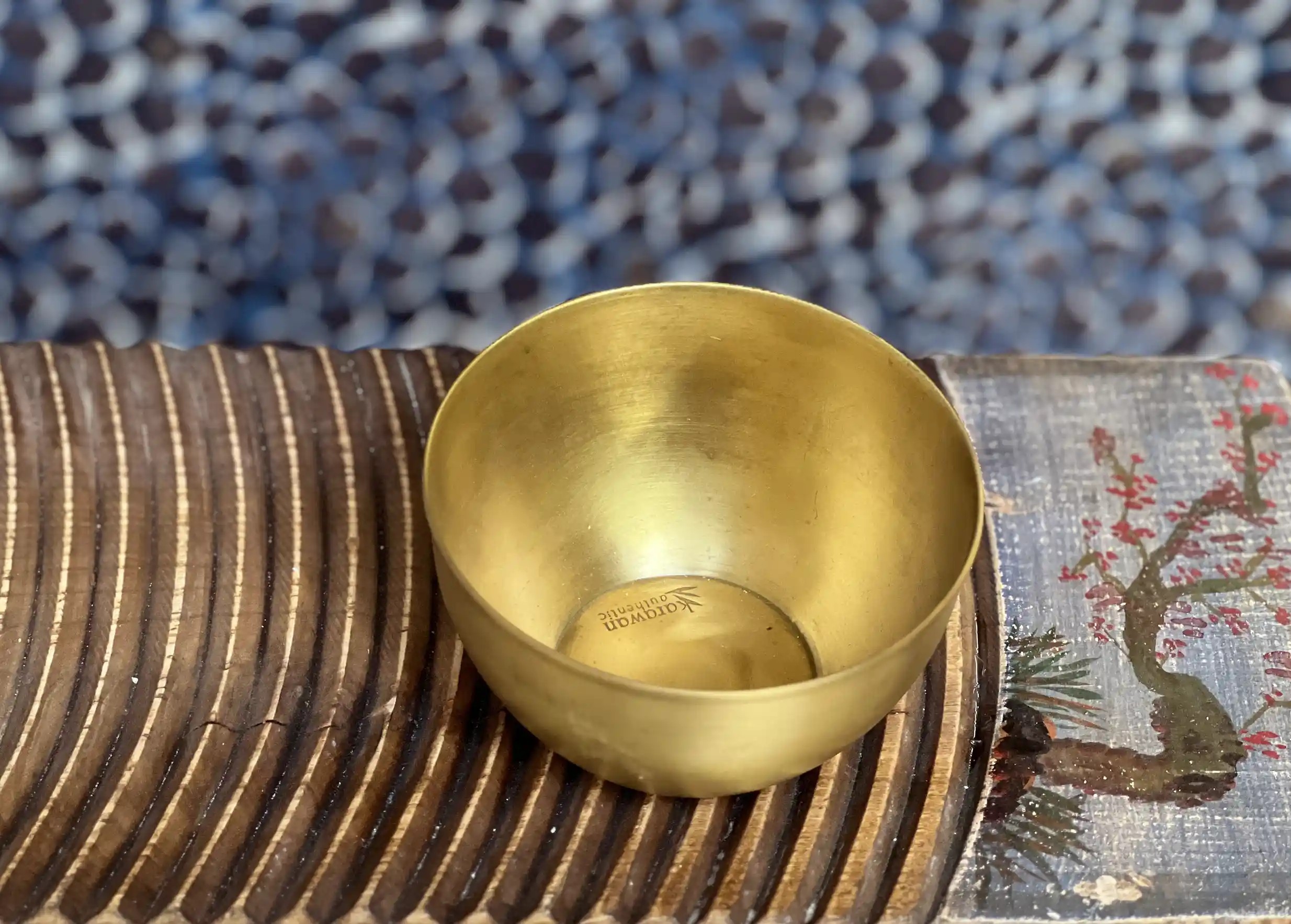 Moon gilded brass bowl, set on a grooved wooden surface, floral illustration on the side