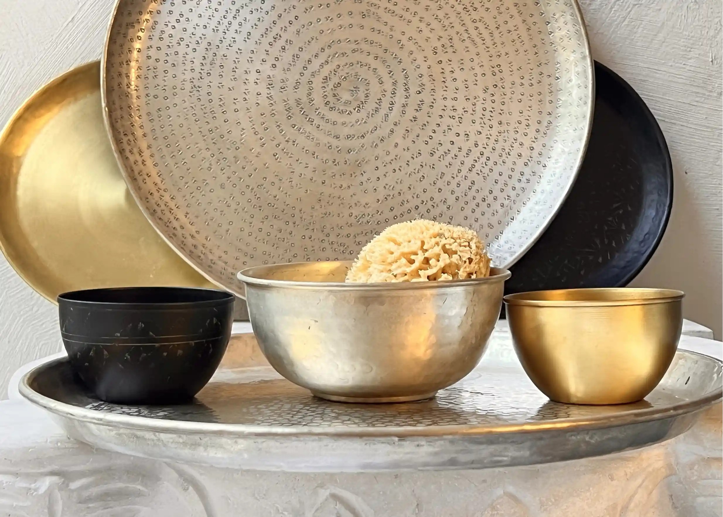 Collection of brass decorative objects, silver-plated brass bowl in the centre, with a sea sponge, trays in the background