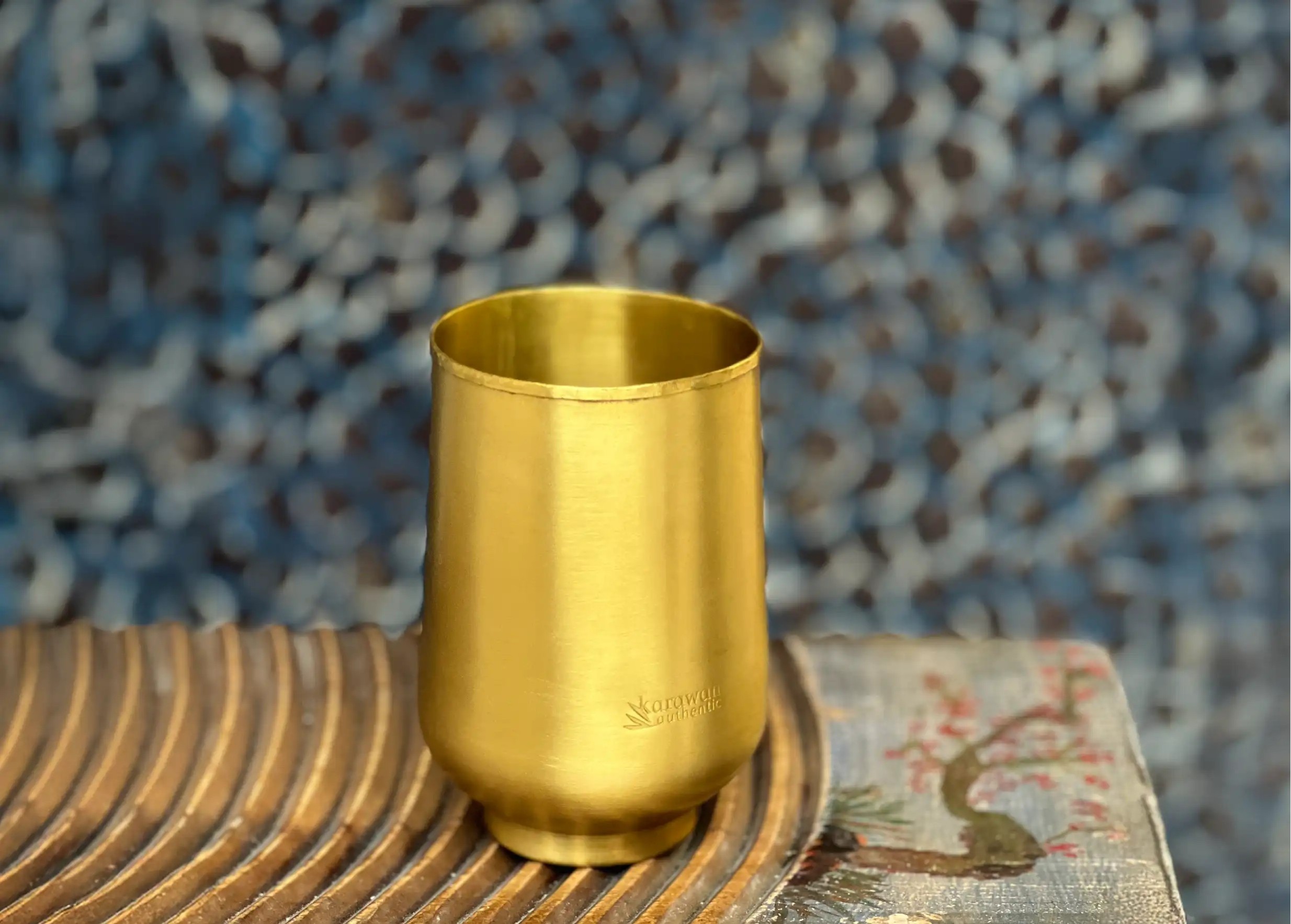 Verre en laiton doré lisse Moon posé sur une surface en bois nervurée, de la marque Karawan