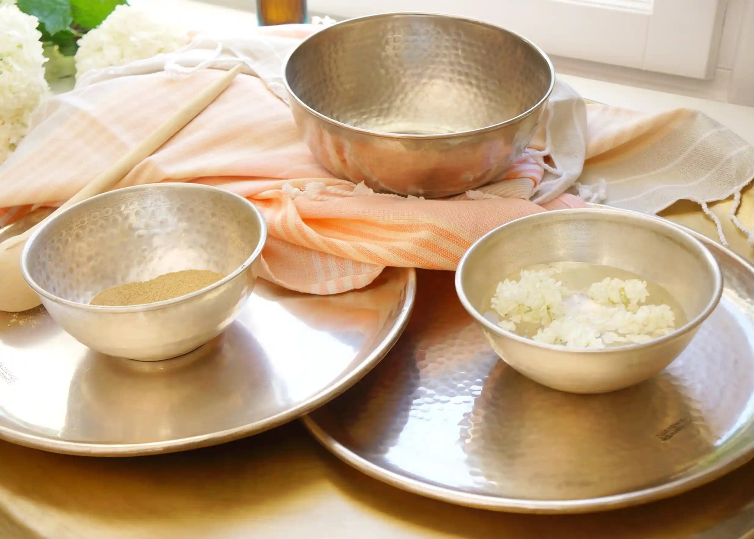 Three brass bowls arranged on silver trays, containing preparations for hammam rituals