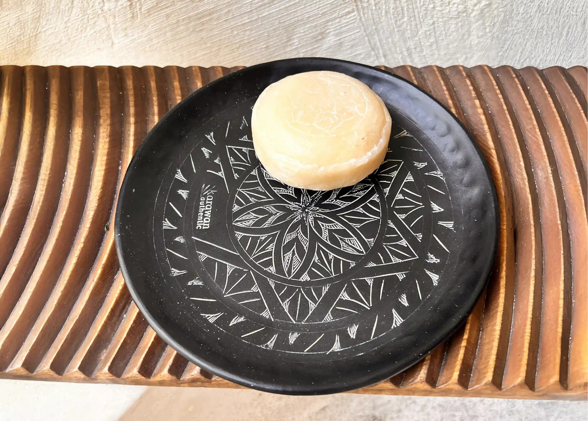 Savon ayurvédique Karawan posé sur une coupelle noire en laiton oxydé et gravé Arabesk, posé sur une surface en bois texturée