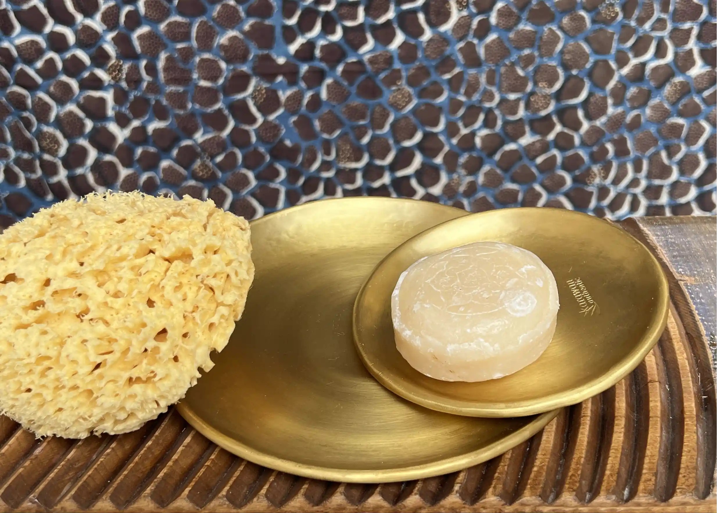 Gold-plated brass bowls with ayurvedic soap and natural sea sponge, set on a textured wooden surface