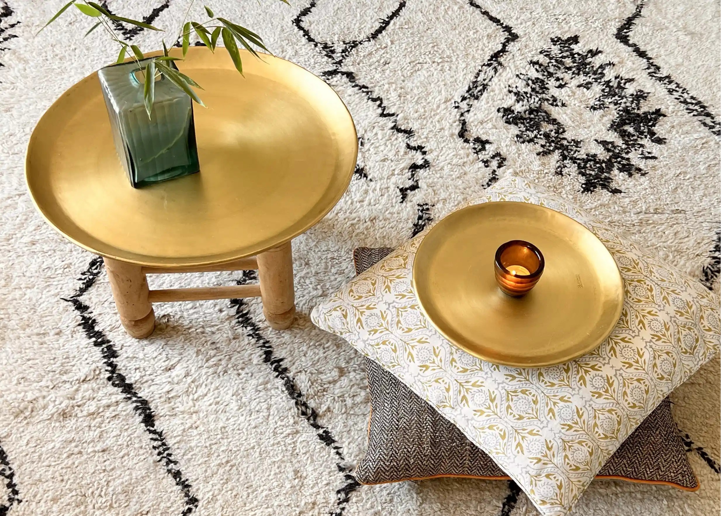 Two gilded brass dishes of various sizes, placed on a cushion and a stool.