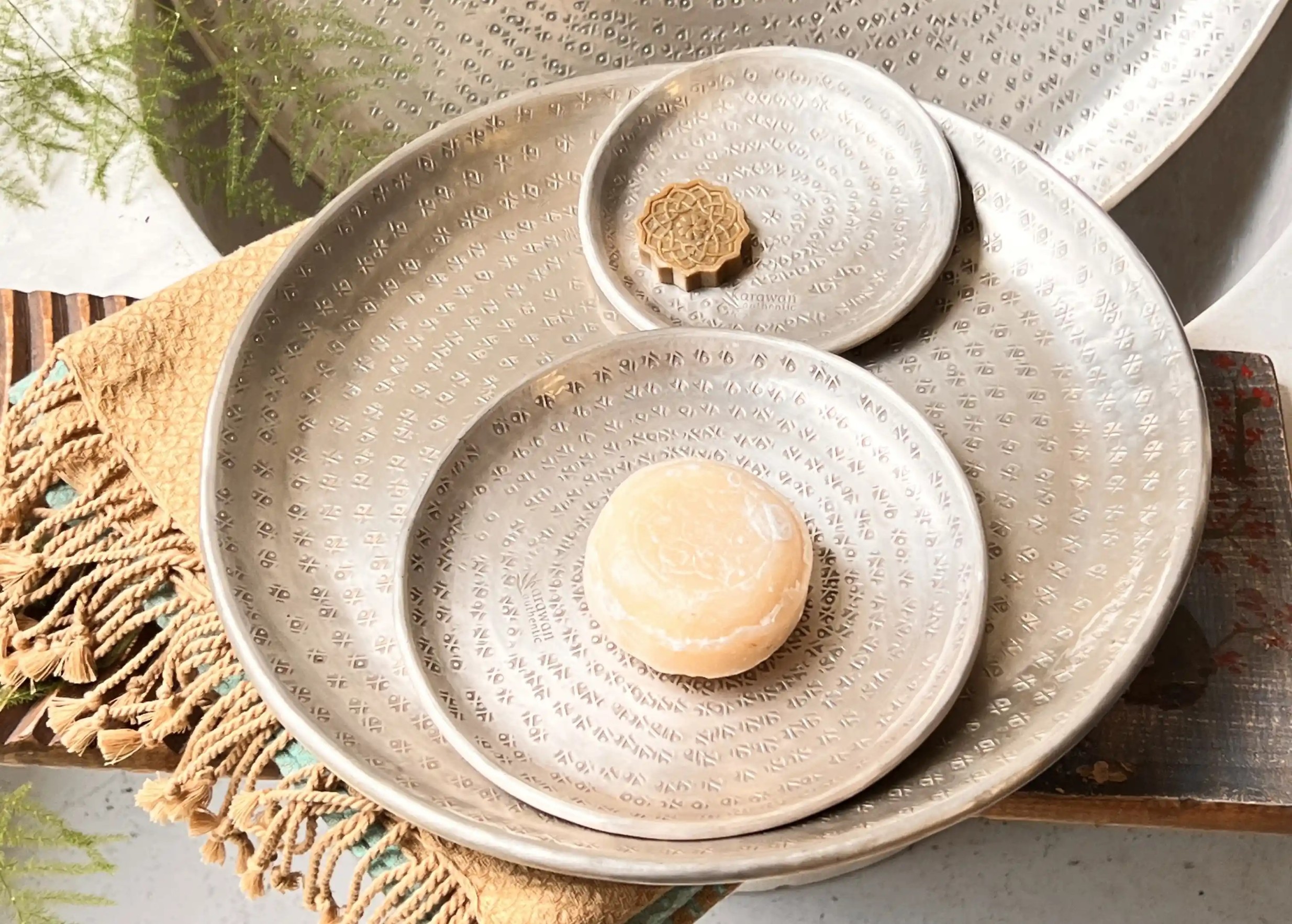 100g Ayurvedic soap with a natural composition in the centre of a silver-coloured dish, placed on a bath fouta.