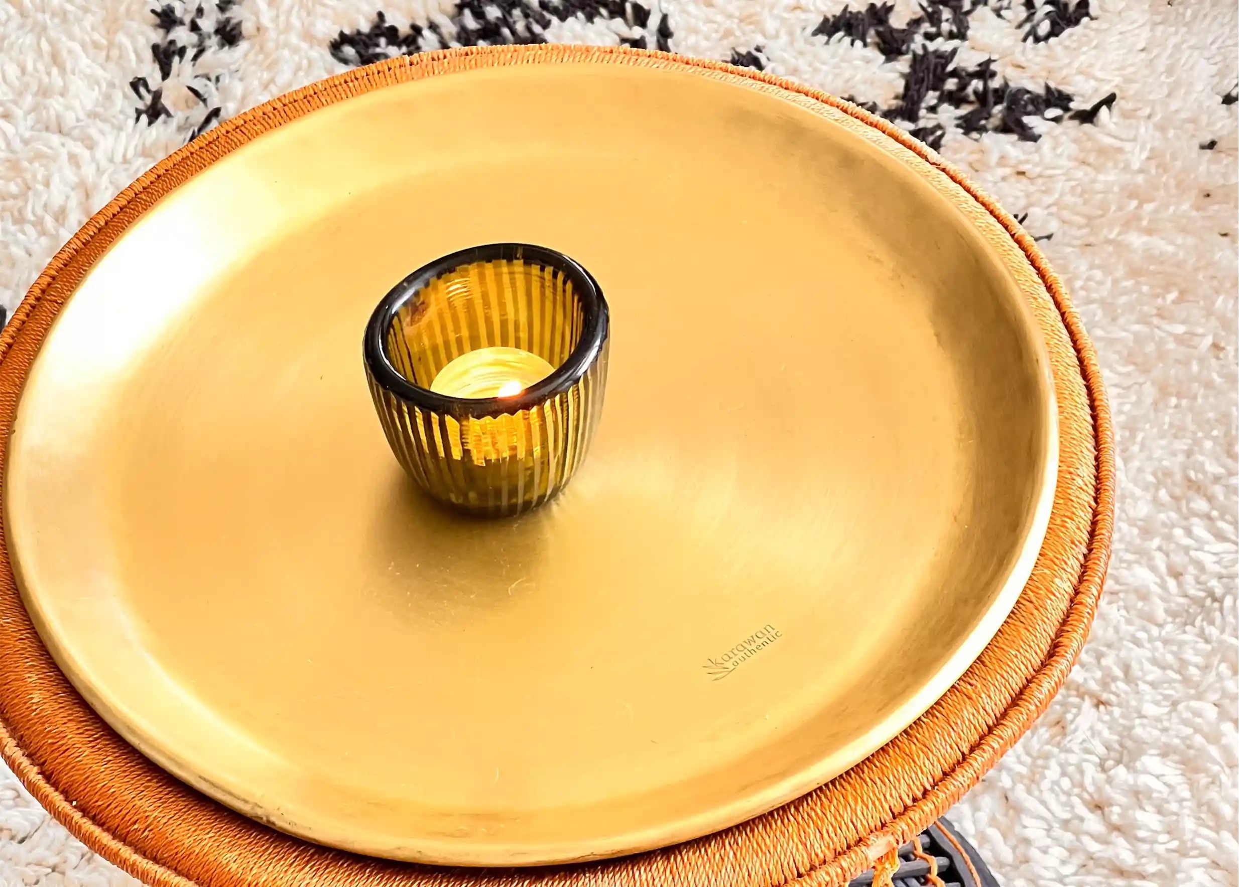 Photophore couleur cactus contenant une bougie allumée, au centre d'un plateau en laiton doré Moon