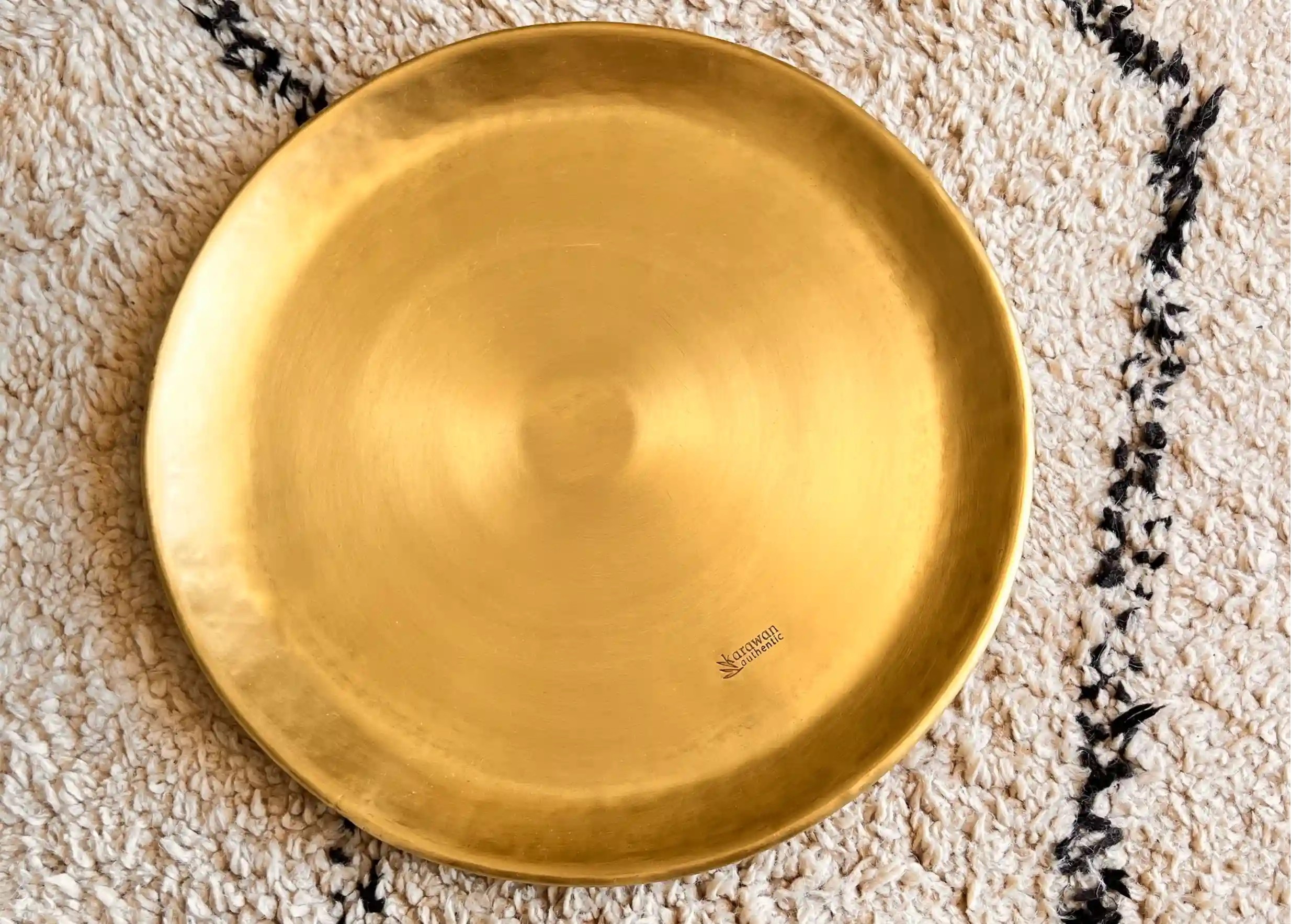 Coupelle en laiton lisse doré sur un tapis aux motifs noirs et blancs, photo prise de haut