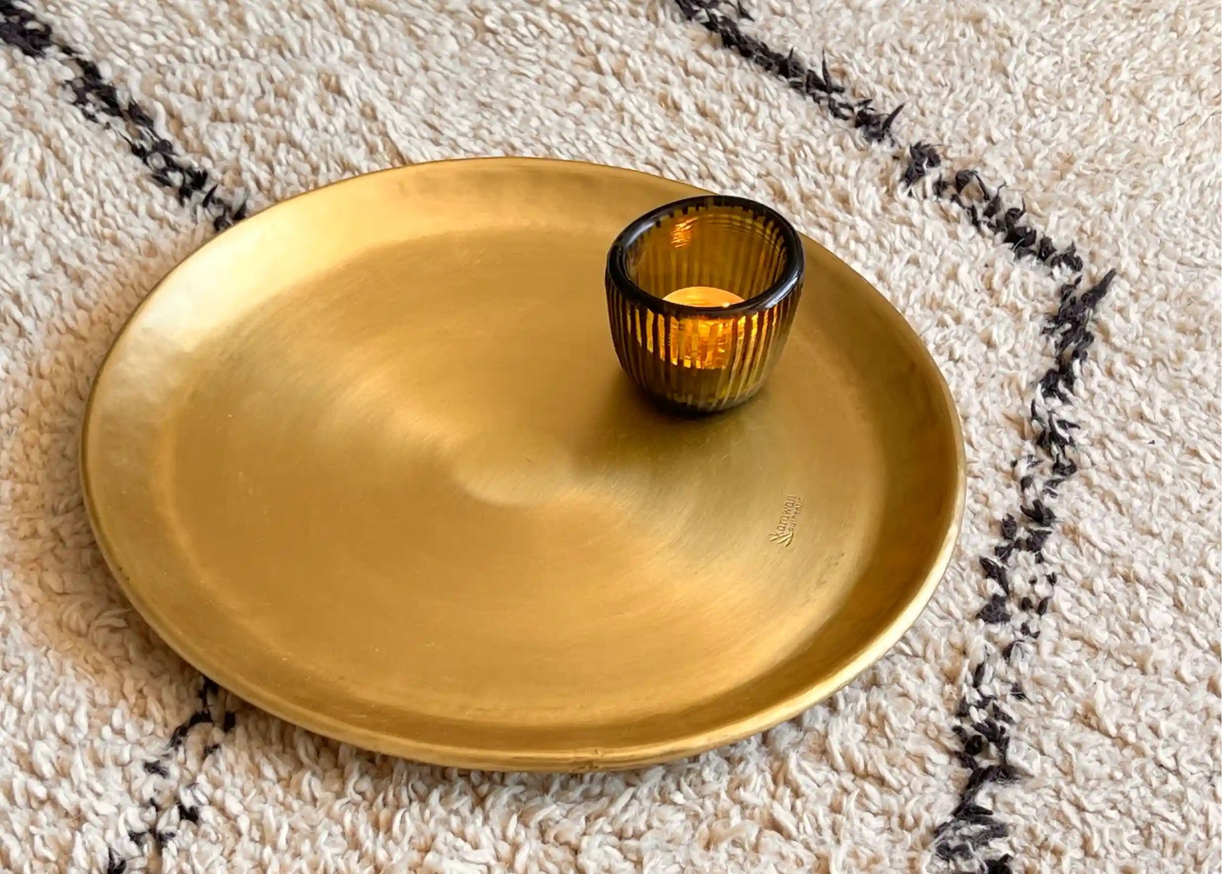 Photophore cactus contenant une bougie allumée, au centre d'un plateau en laiton doré Moon, un tapis aux motifs noirs et blancs